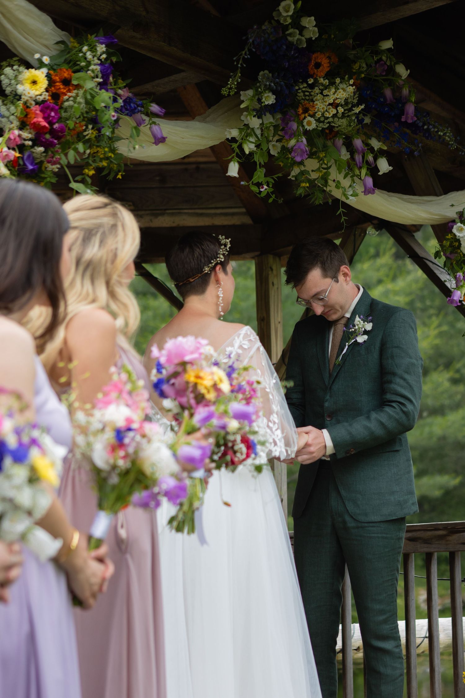 Wedding party gathered under a floral-adorned gazebo during an outdoor ceremony.
