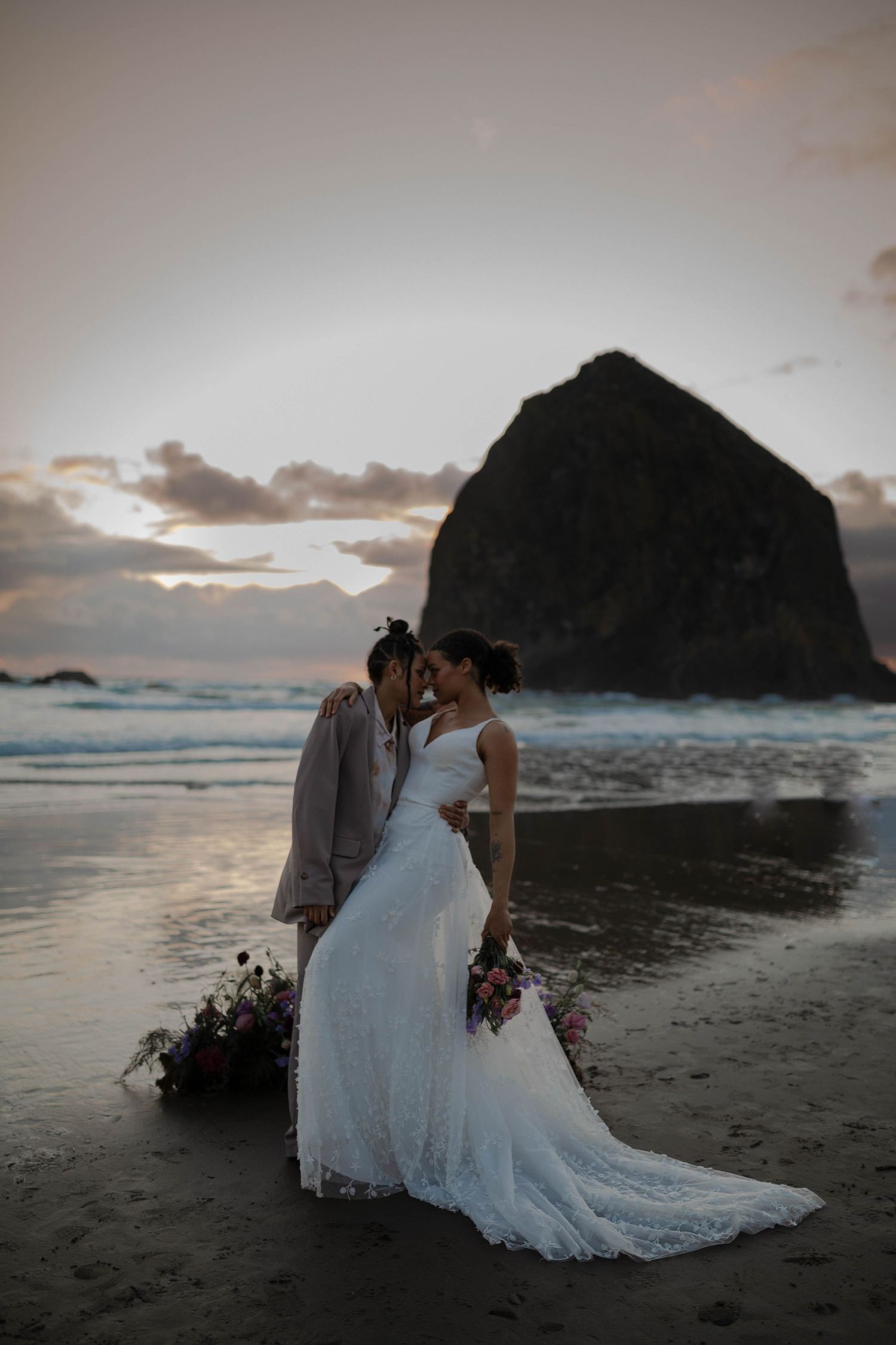 A wedding portrait on Cannon Beach with the dramatic silhouette of Haystack Rock against a sunset sky.