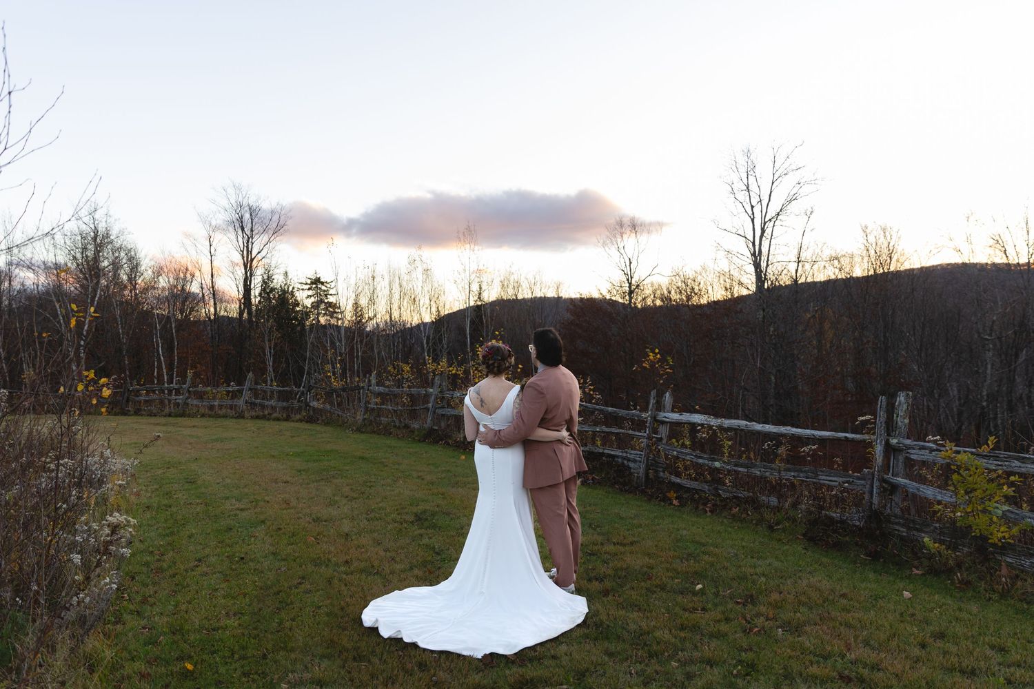 Wedding couple embraces against rustic fence during golden sunset.