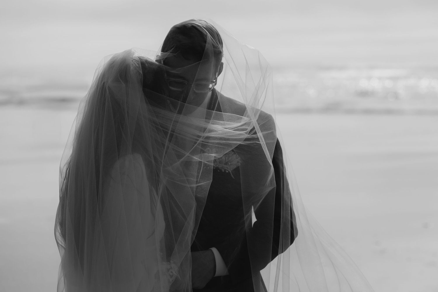 Black and white image of a silhouetted figure walking along a misty beach at sunset.