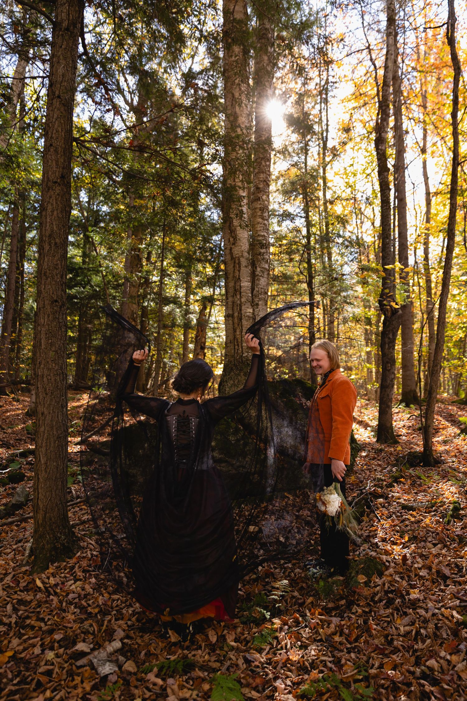 Hunters in orange safety vests walk through autumn forest with fallen leaves and tall trees at sunset.