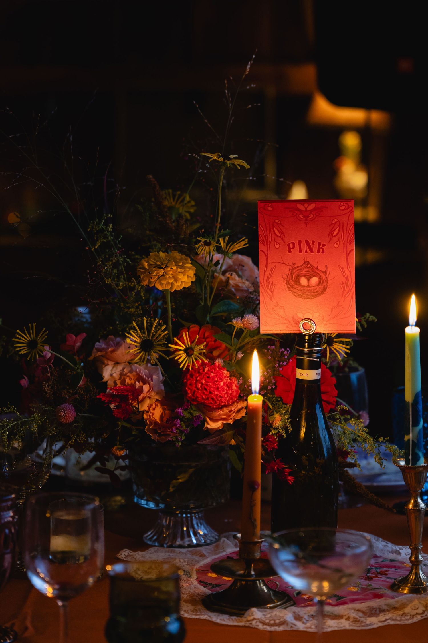 Elegant wedding table with red floral centerpiece, candles, and glowing table number card.