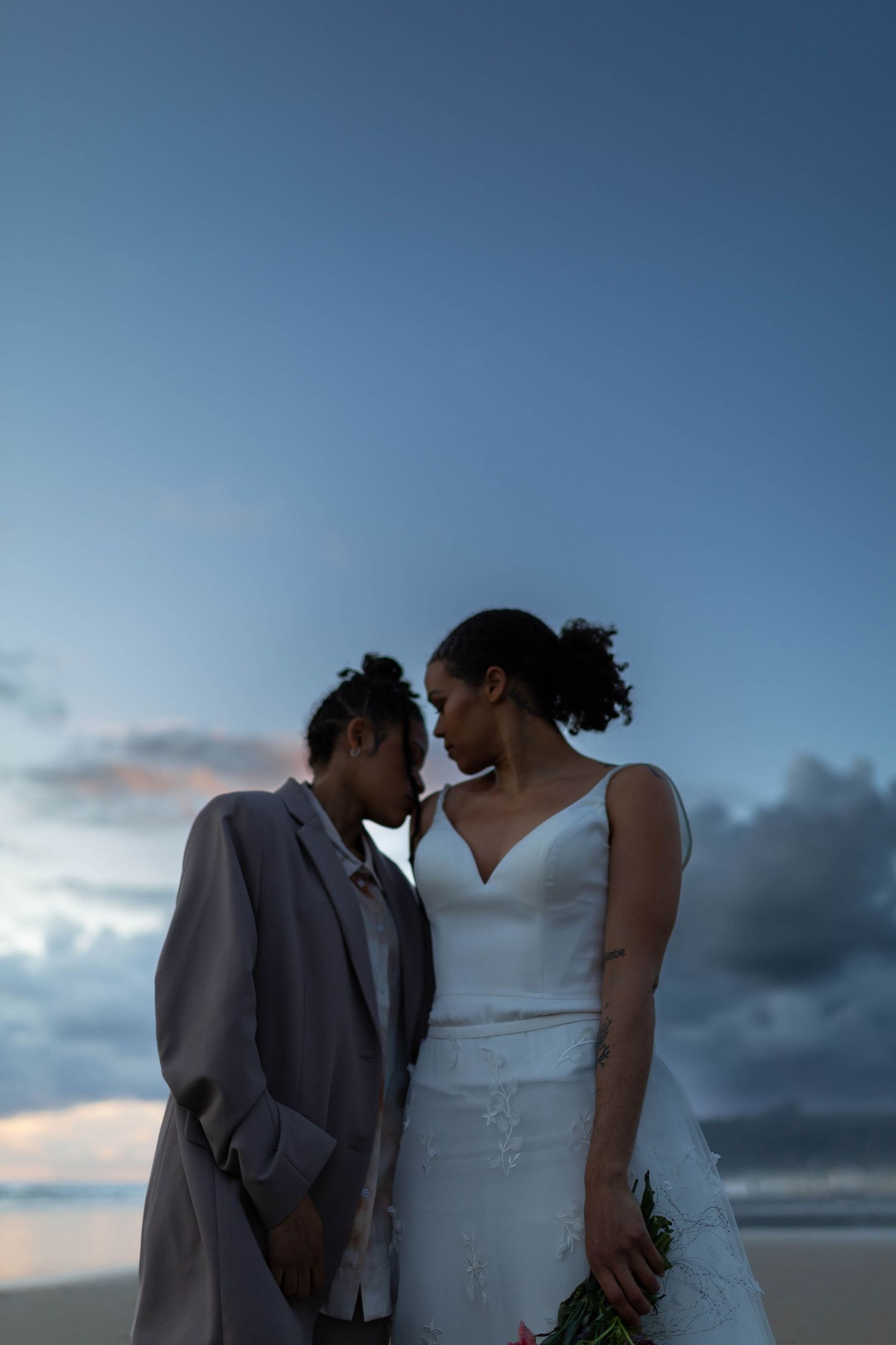 A tender moment between newlyweds against a dusky blue sky at the beach.