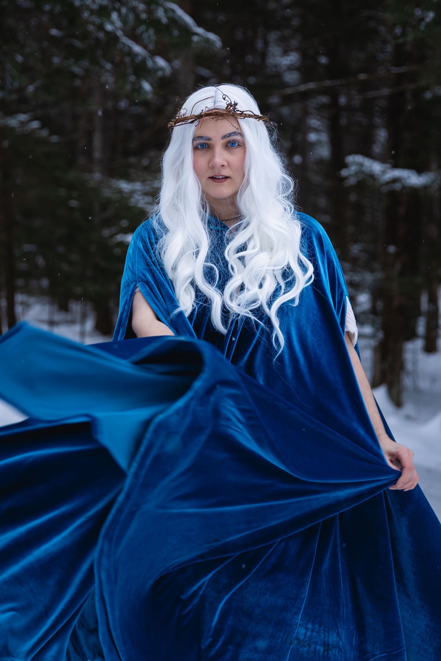 Woman with white hair wearing blue velvet gown and crown in snowy forest.