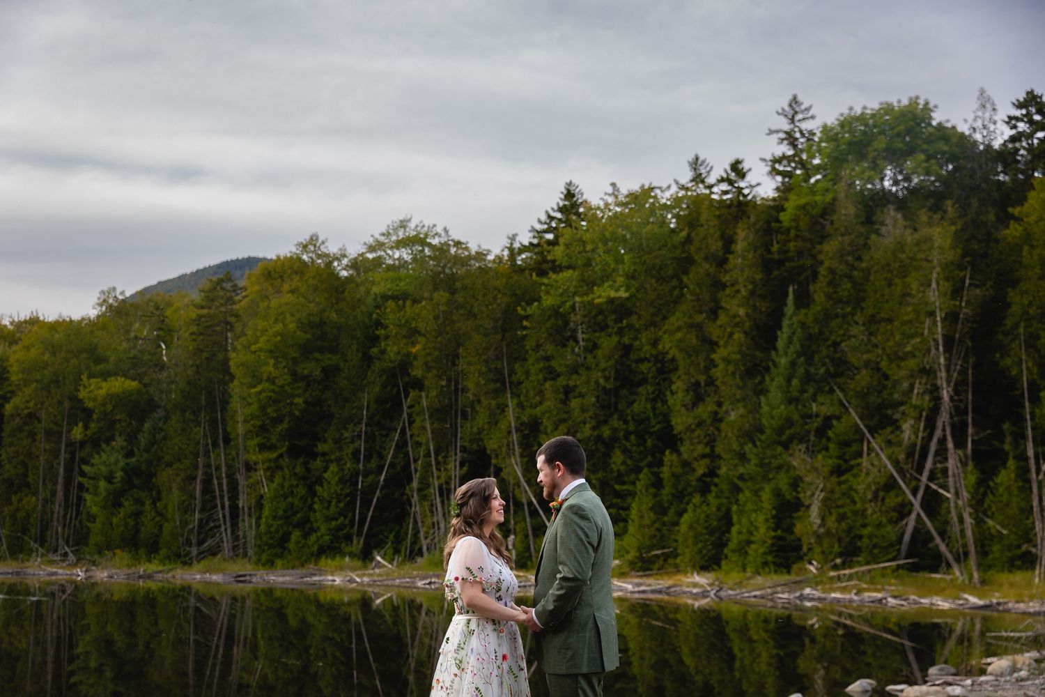 Bride and groom share intimate moments during their wedding photoshoot on a scenic lakeside dock surrounded by forest.