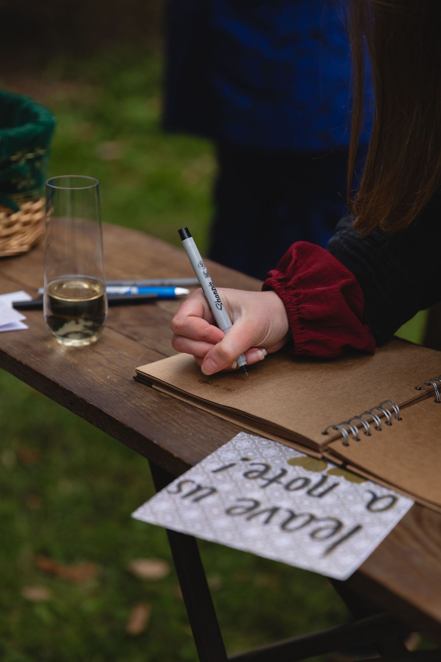 Someone signing a guestbook with a glass of champagne on wooden table.