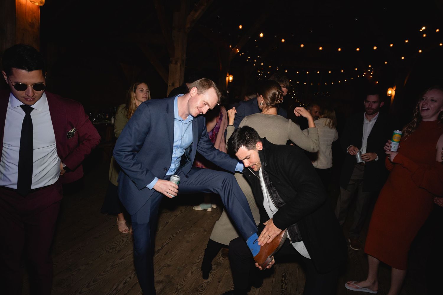 People dancing and celebrating at a nighttime outdoor party with string lights overhead.