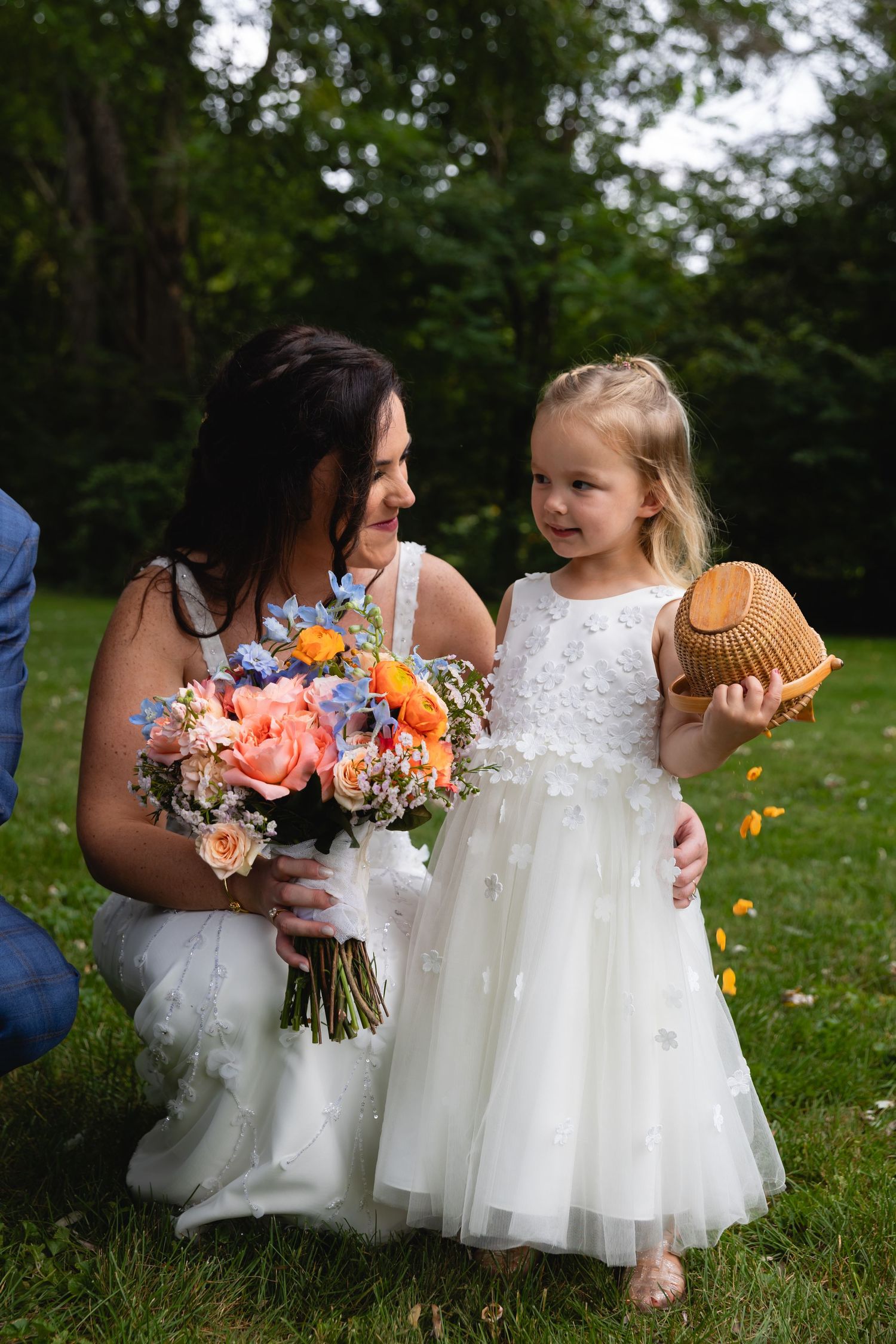 A beautiful spring wedding bouquet with coral and blue flowers held on a grassy lawn with trees in the background.