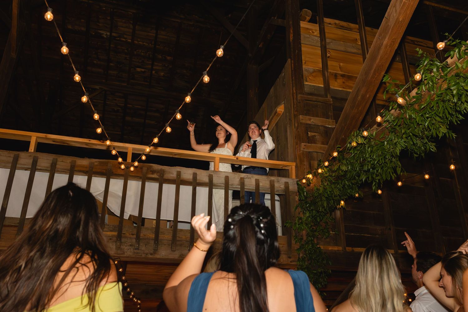 Guests looking up at outdoor party deck decorated with string lights as shoes dangle over railing.