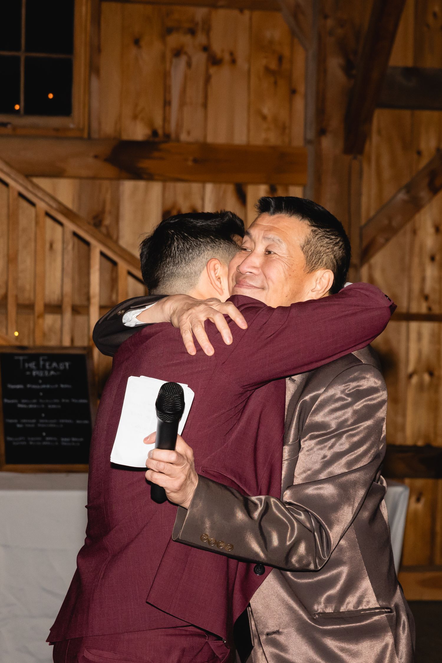 Two people sharing an emotional embrace at what appears to be a rustic wooden barn venue.