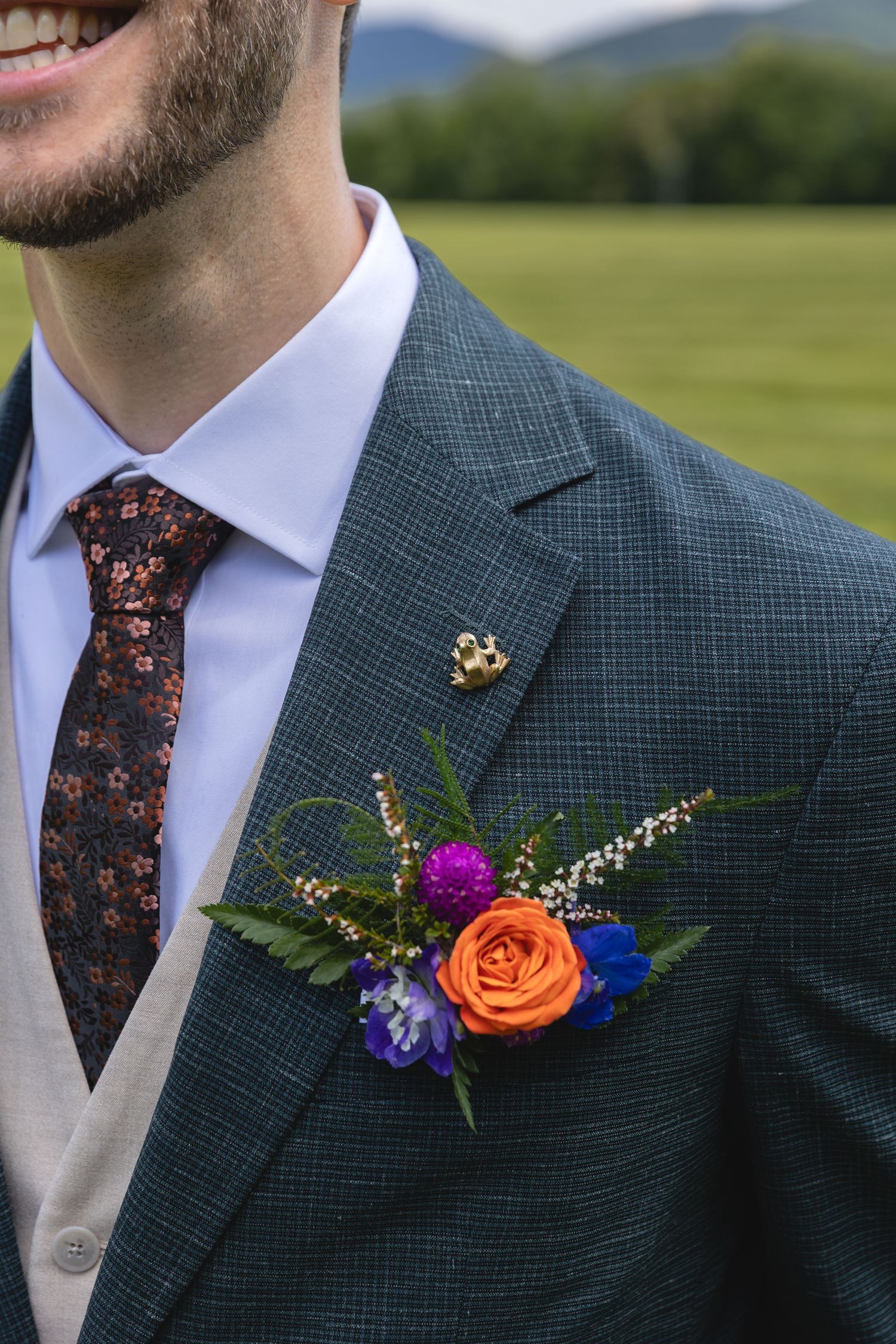 Close-up of a vibrant orange and blue boutonniere on a textured grey suit jacket.