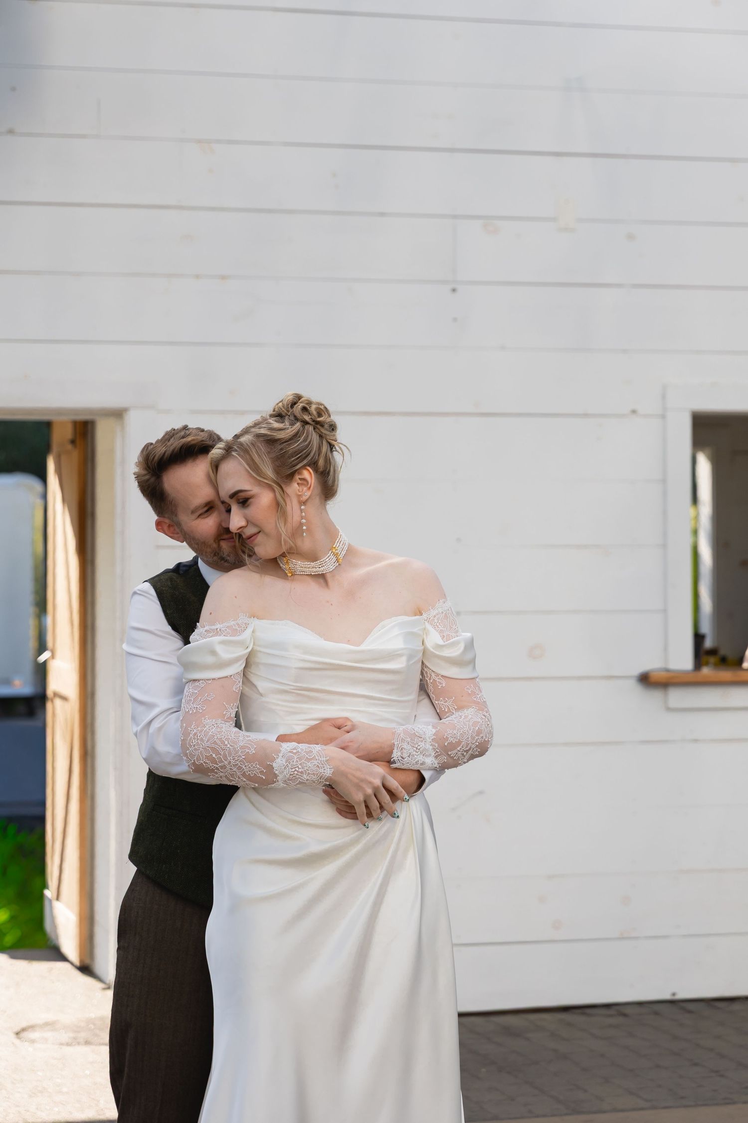 A romantic wedding couple embraces and dances together outside a white building in elegant attire.