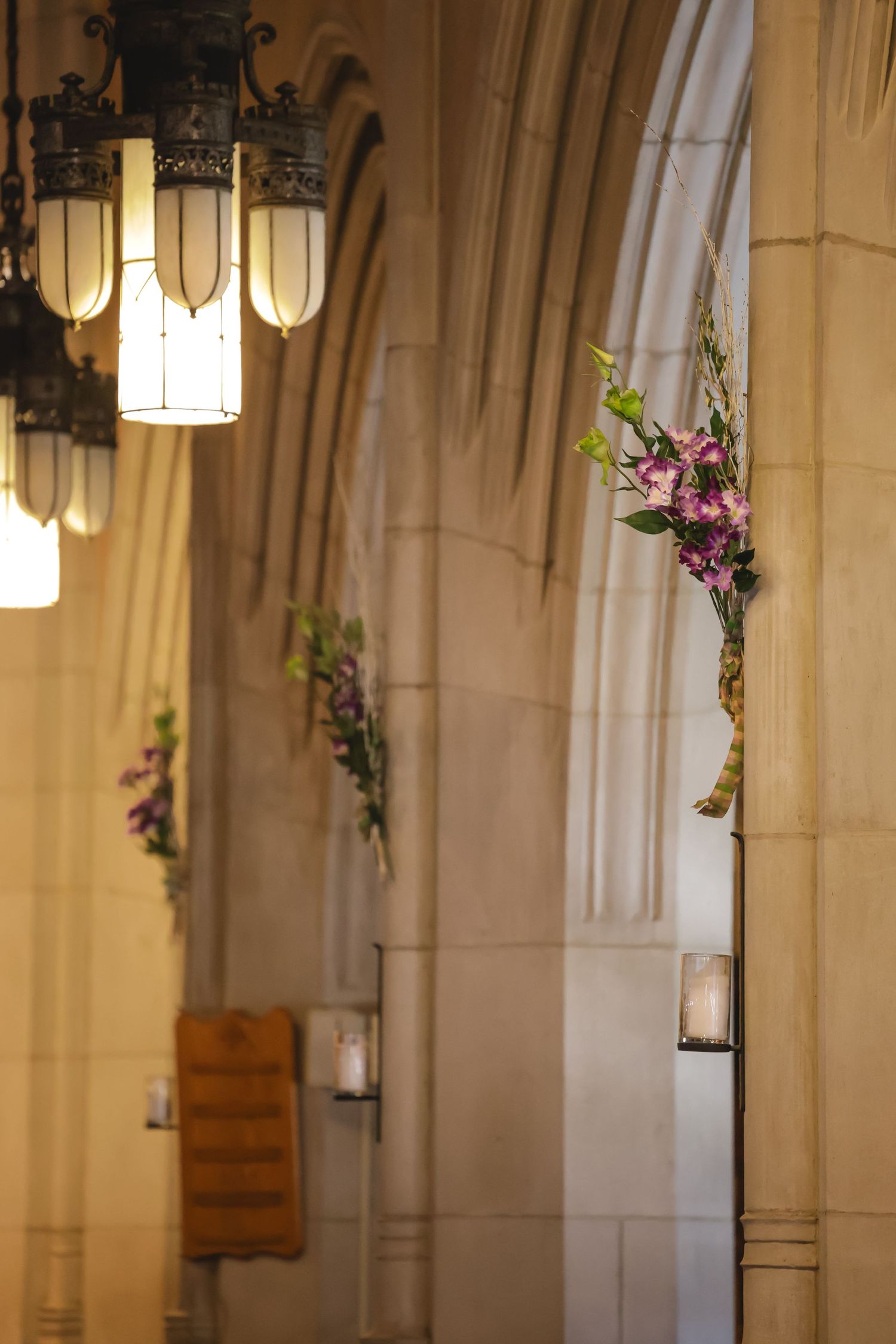 Elegant church interior with hanging pendant lights and stone columns decorated with purple floral arrangements.