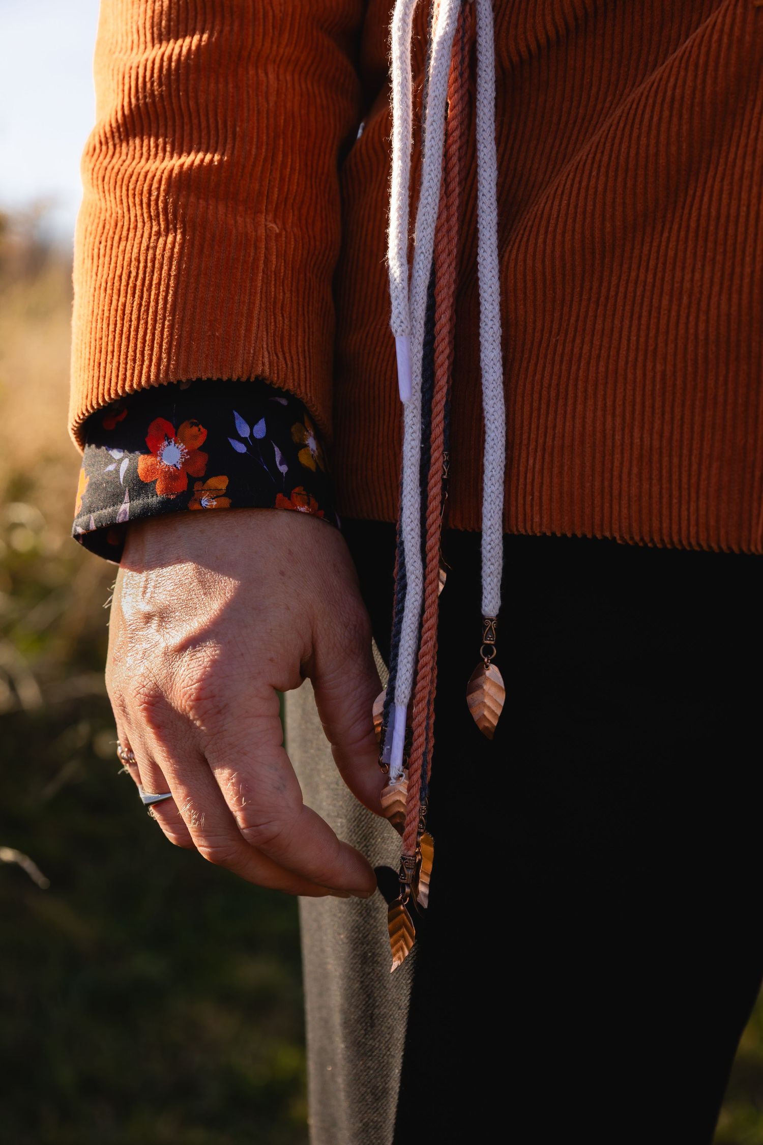 Close-up view of hands holding a colorful friendship bracelet against an orange corduroy background in natural light.