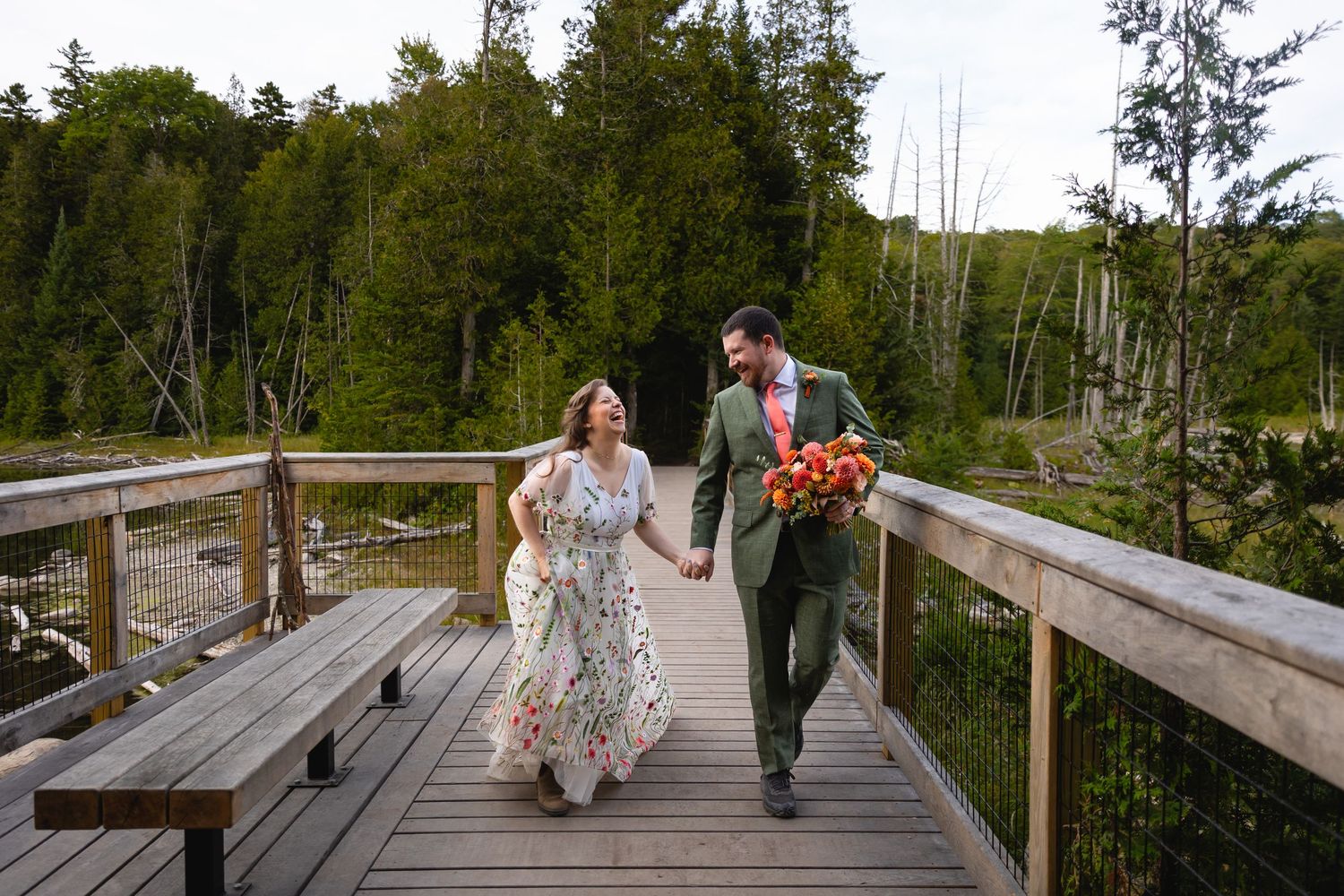 People walking along a wooden boardwalk trail through a scenic forest landscape.