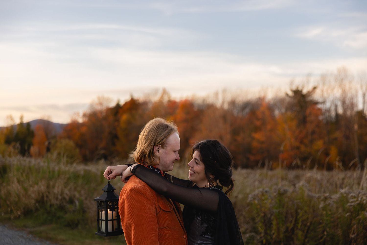 Couple sharing tender moments in autumn field with golden light and fall foliage in the background.
