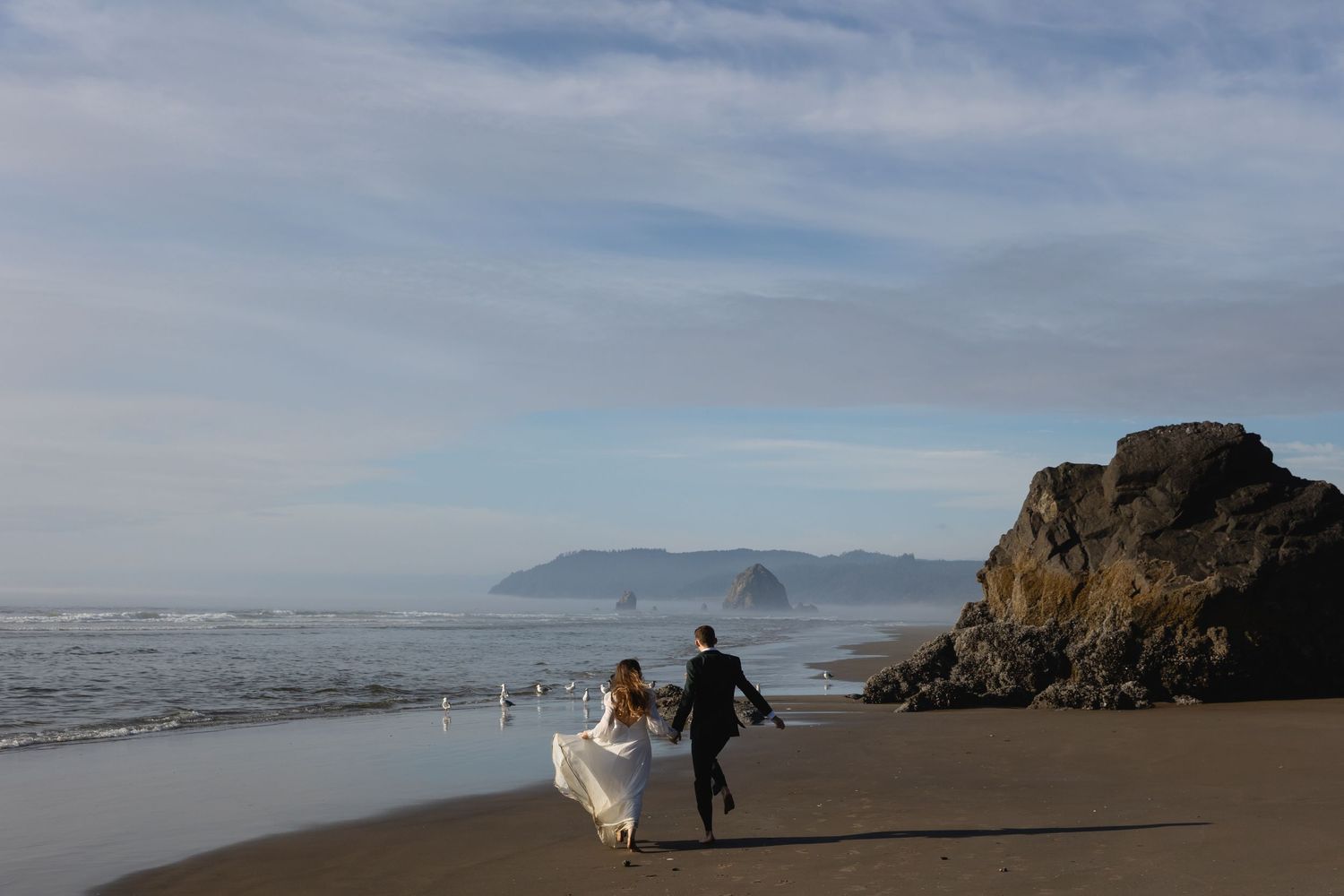 Scenic coastal beach landscape with rugged cliffs and misty mountains in the distance along the Pacific Ocean.