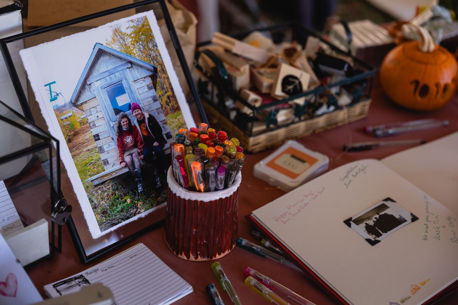 A framed photograph sits on a desk next to a decorated red cake and scattered papers with a pumpkin in the background.