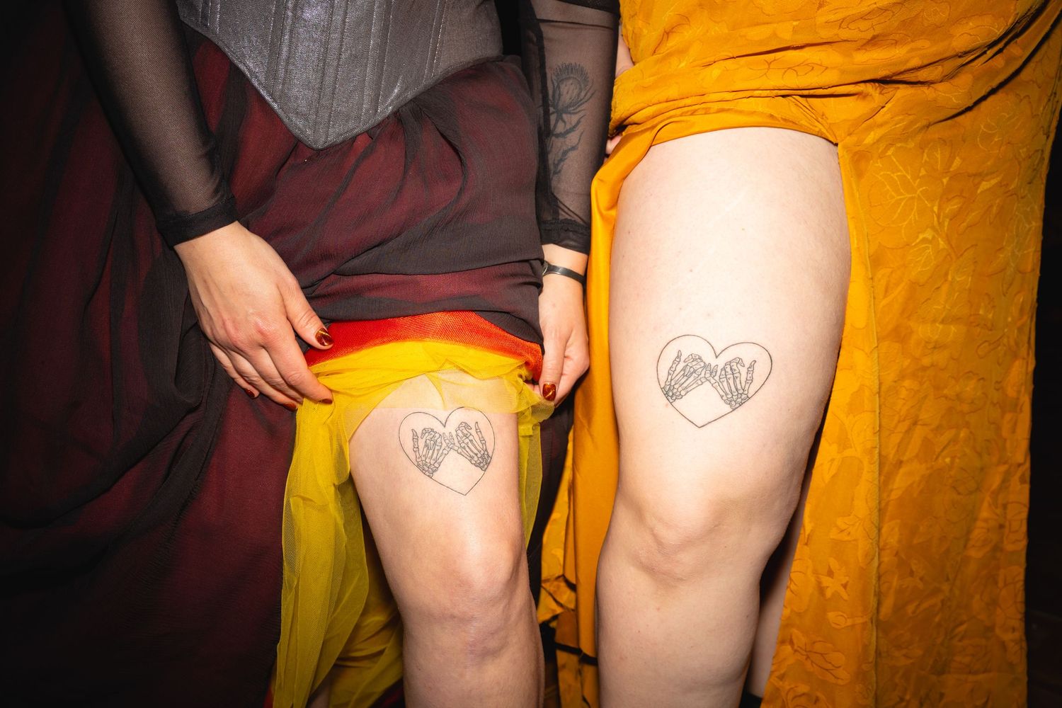 Two people showing matching heart tattoos on their knees while wearing yellow and burgundy clothing.