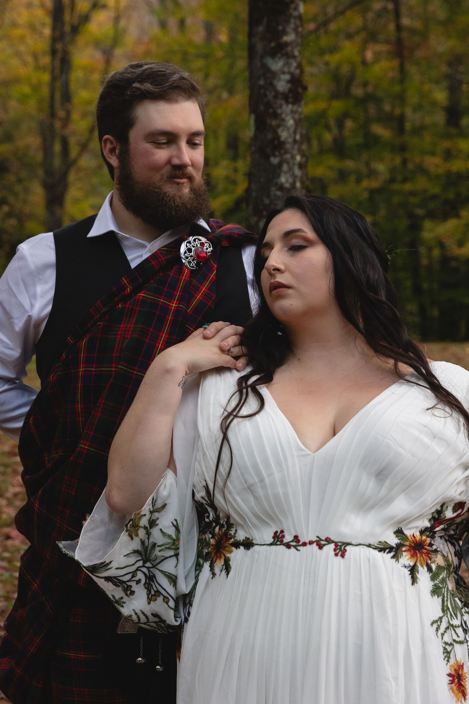 A gentle moment between newlyweds featuring Scottish and nature-inspired wedding attire in a forest setting.