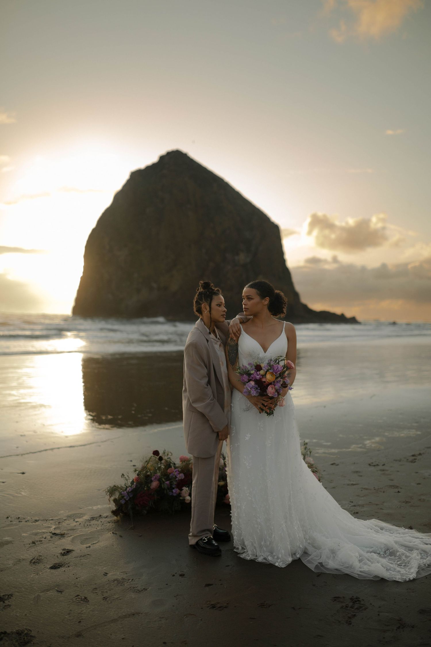A wedding couple shares an intimate moment on Cannon Beach during golden hour with Haystack Rock in view.