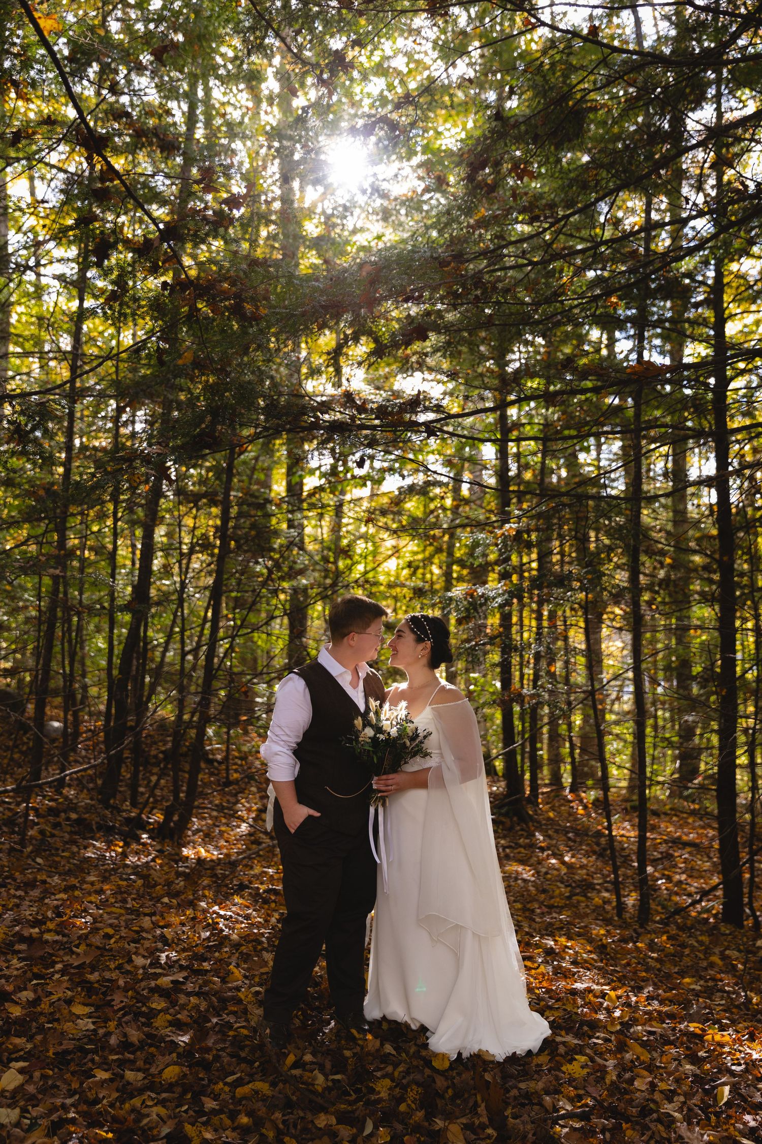 A romantic wedding portrait in a forest with sunlight streaming through autumn trees.