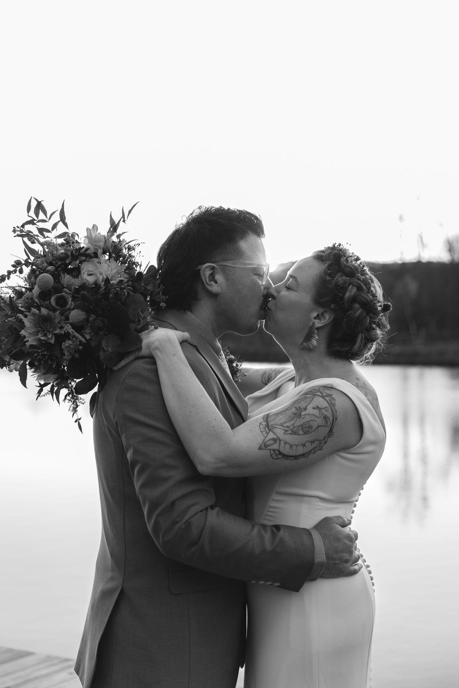 Intimate black and white portrait of couple sharing romantic moment with bouquet by lake.