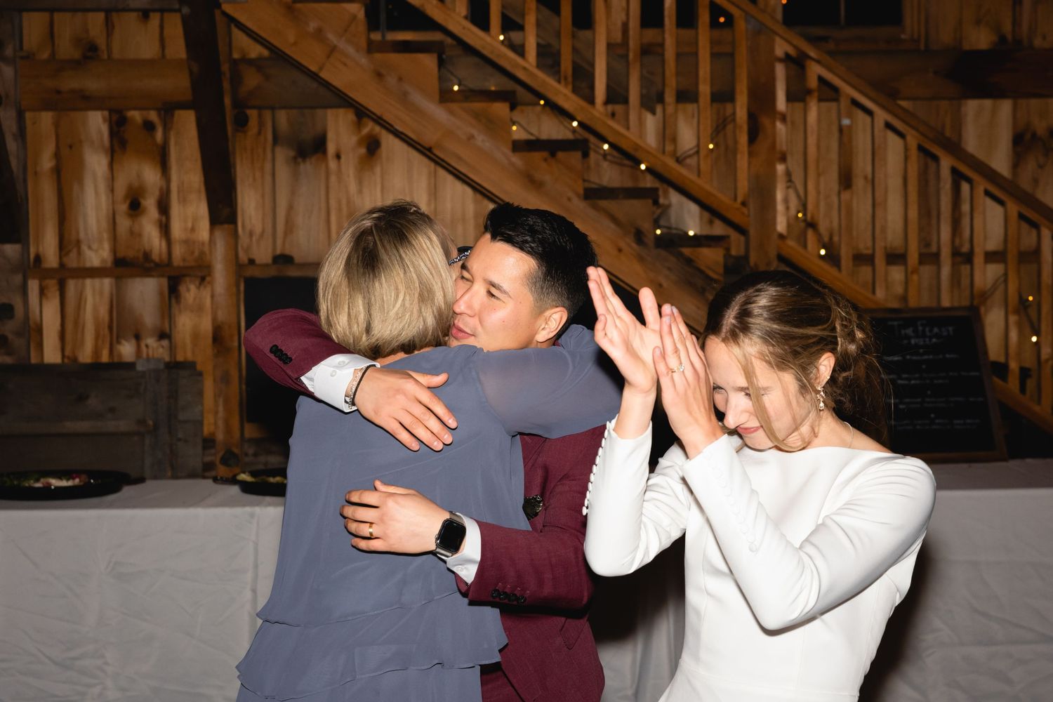 People celebrating at a rustic barn reception venue with wooden staircase in the background.