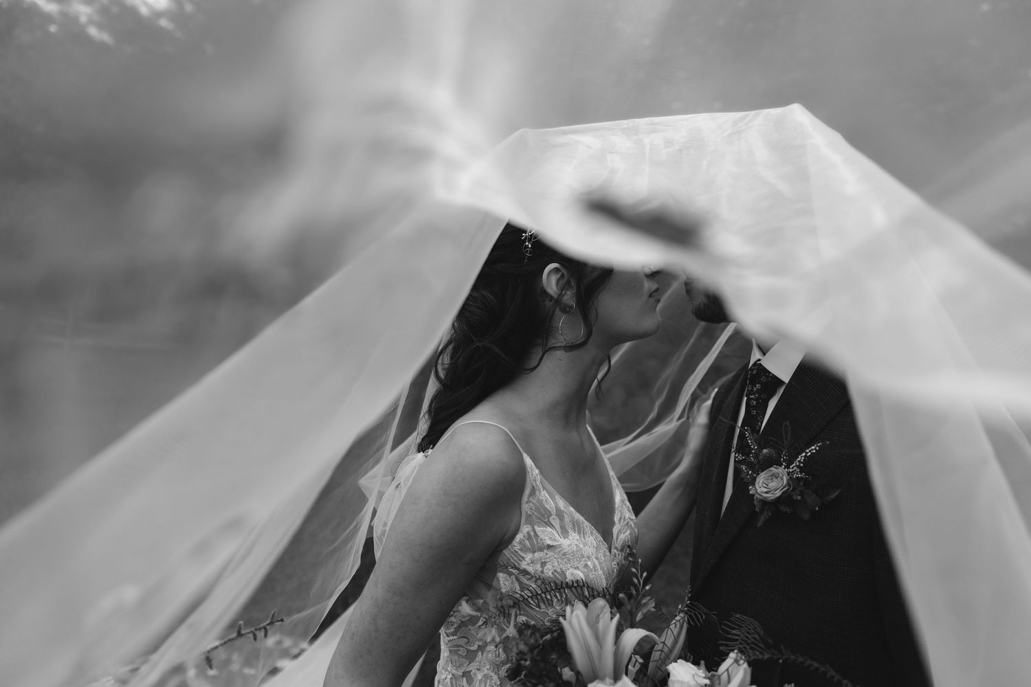 Black and white intimate moment captured under flowing wedding veil.