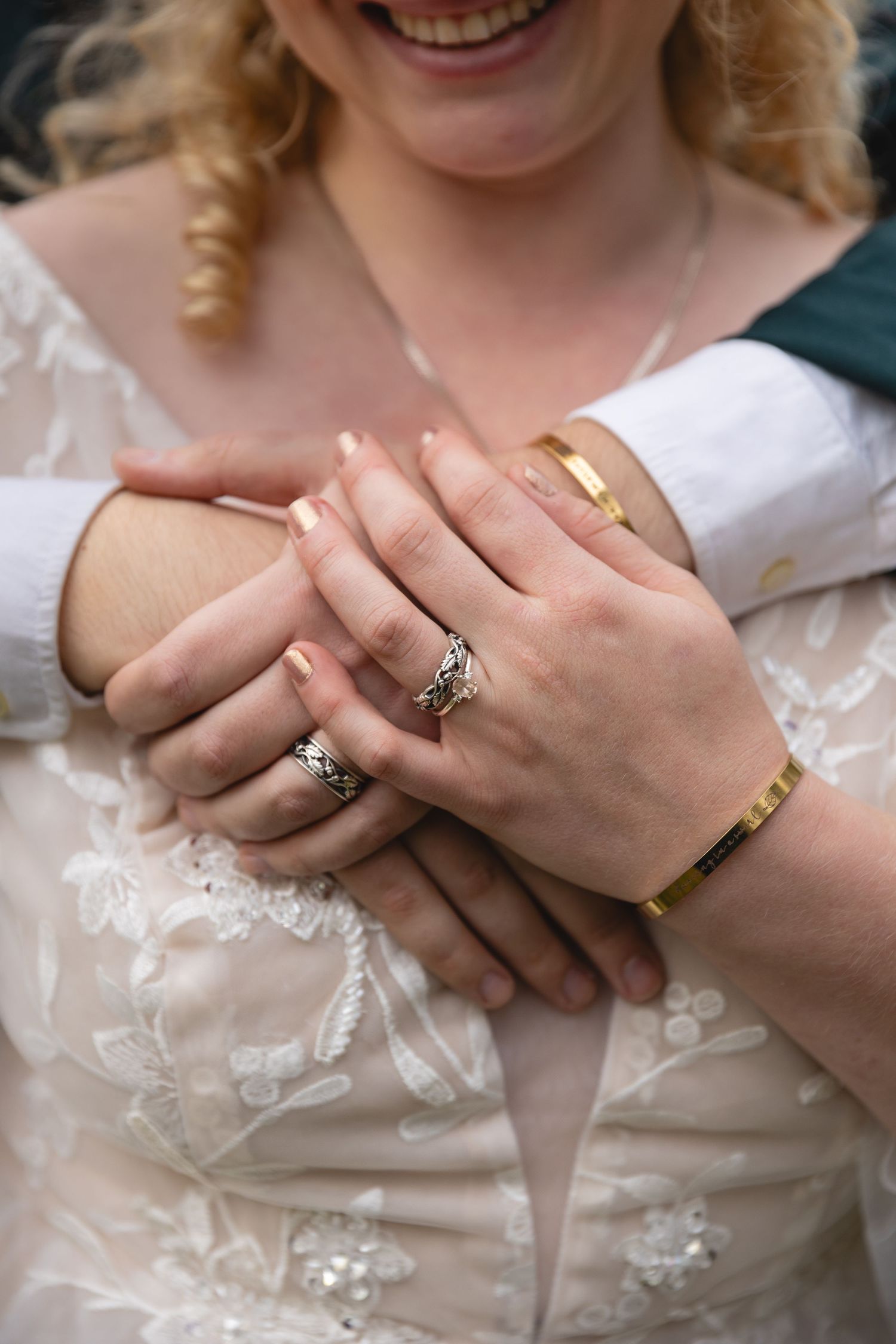 Close-up of hands wearing delicate rings and lace dress details during a wedding celebration.