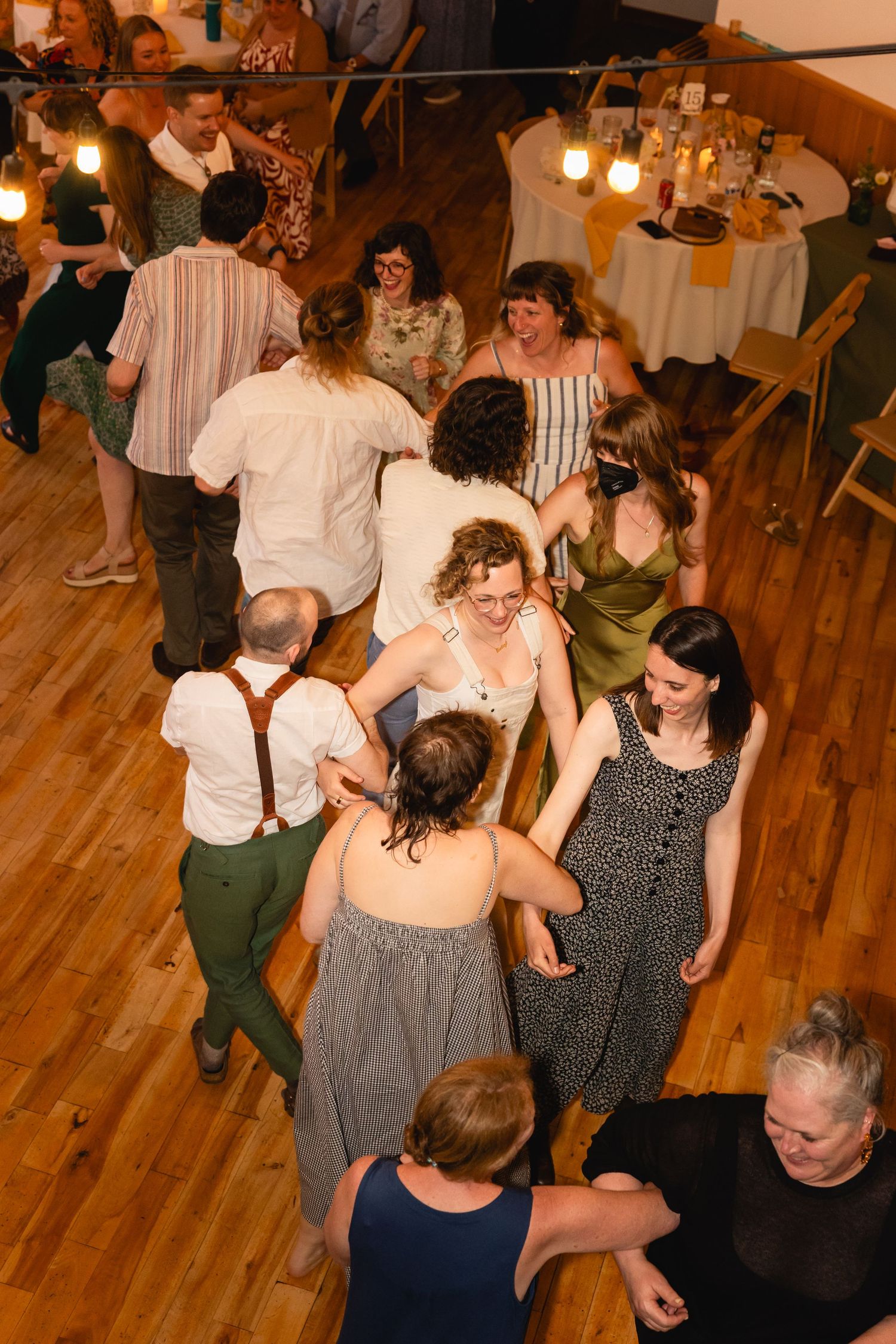 People dancing and socializing at a lively gathering on a wooden dance floor in warm lighting.