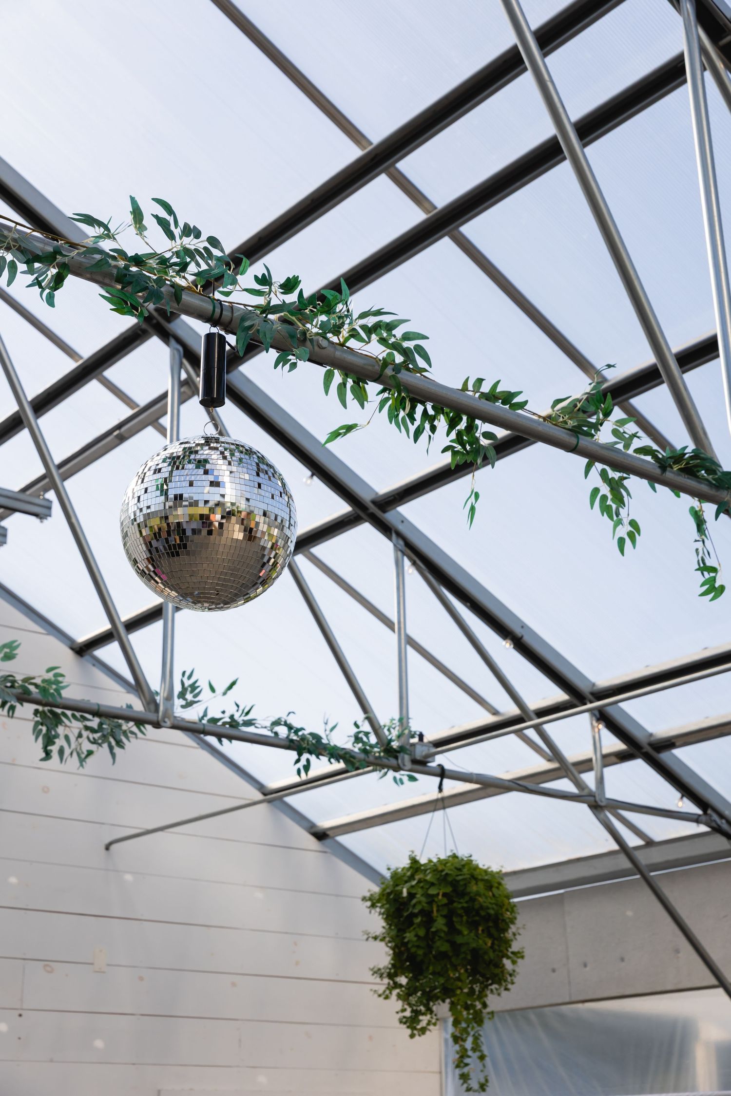 Glass ceiling structure with hanging disco ball and green foliage decorations.