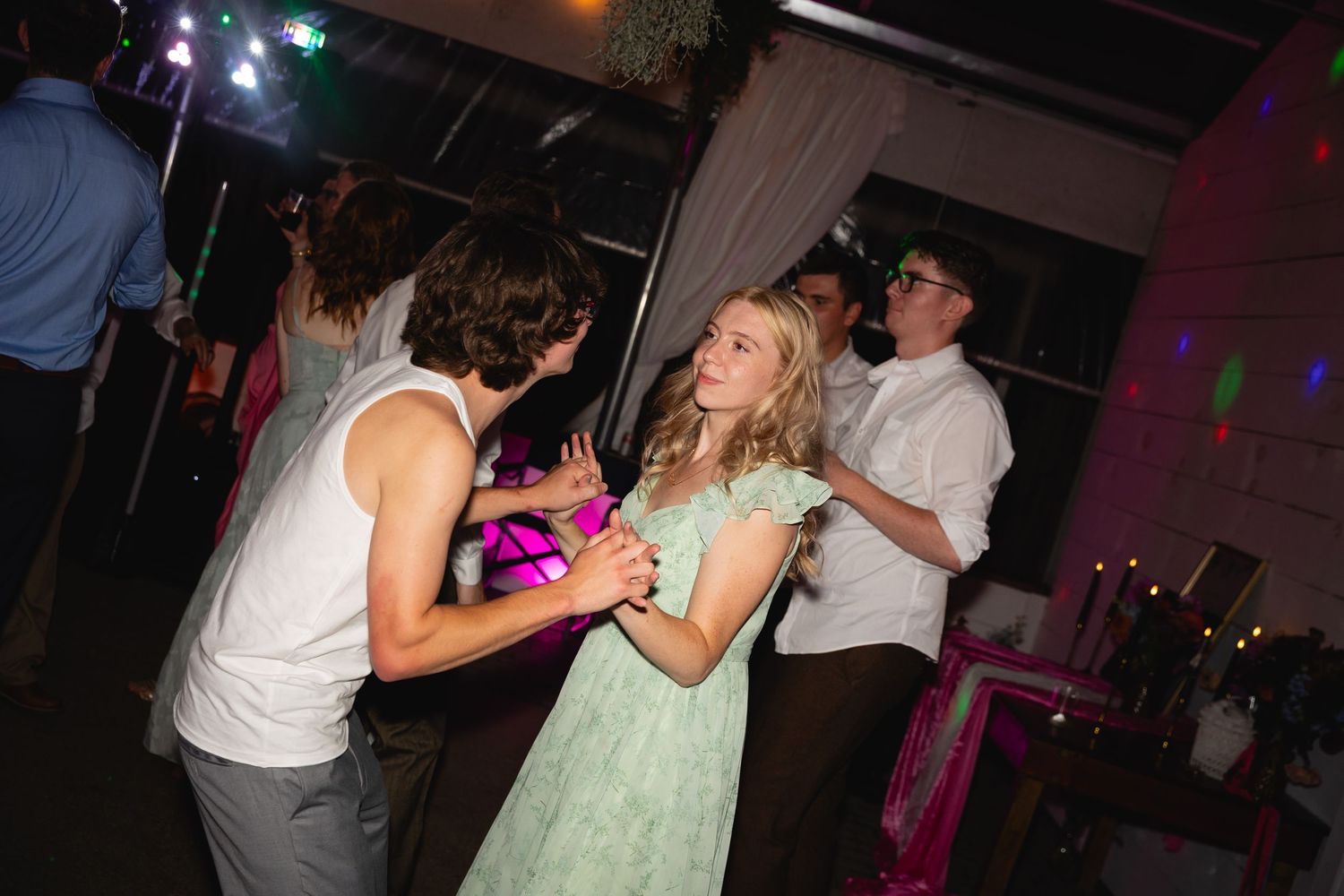 People dancing together at a party with colorful lighting and festive atmosphere.