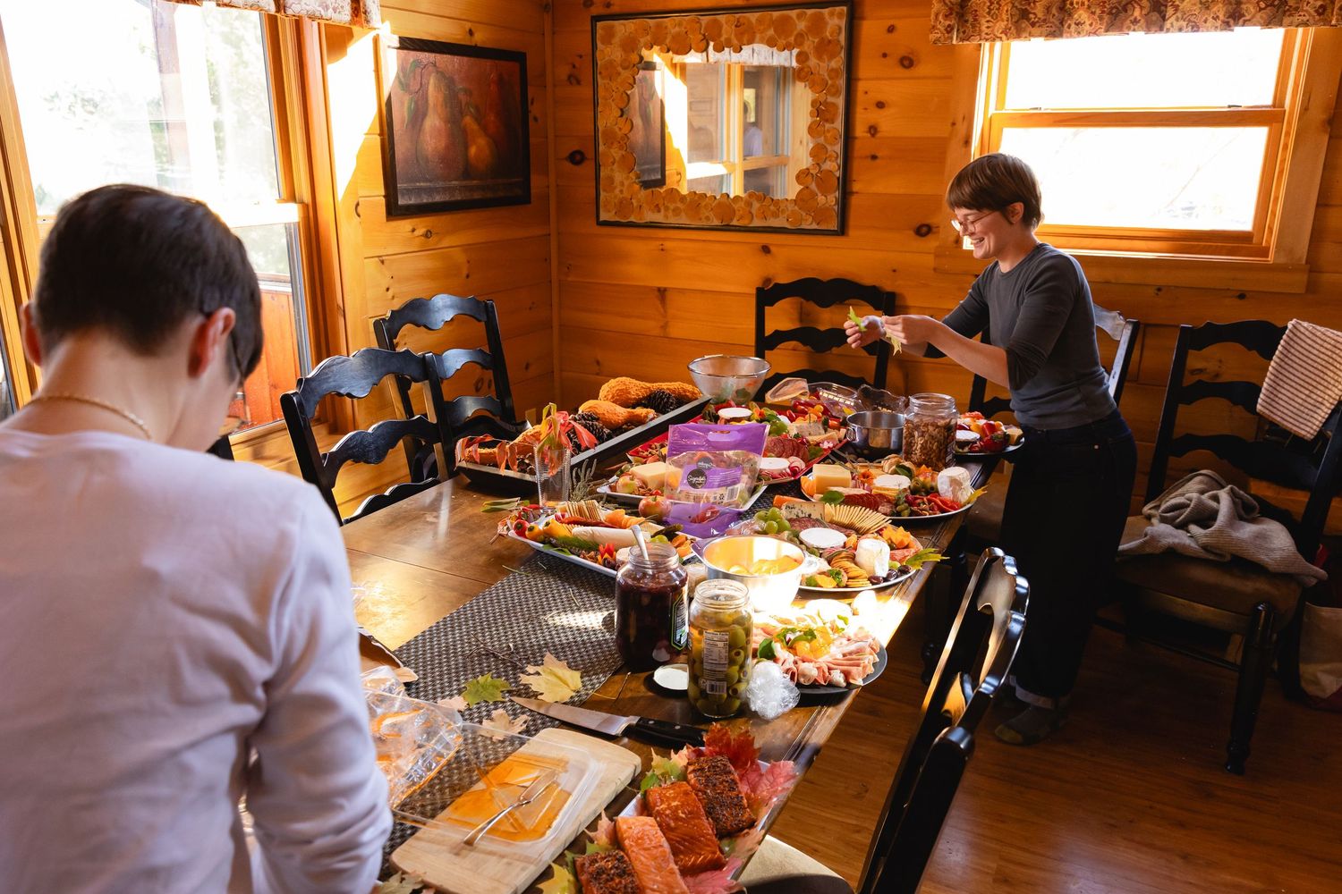 People gather around a wooden table in a cozy cabin interior filled with crafting supplies and creative materials.