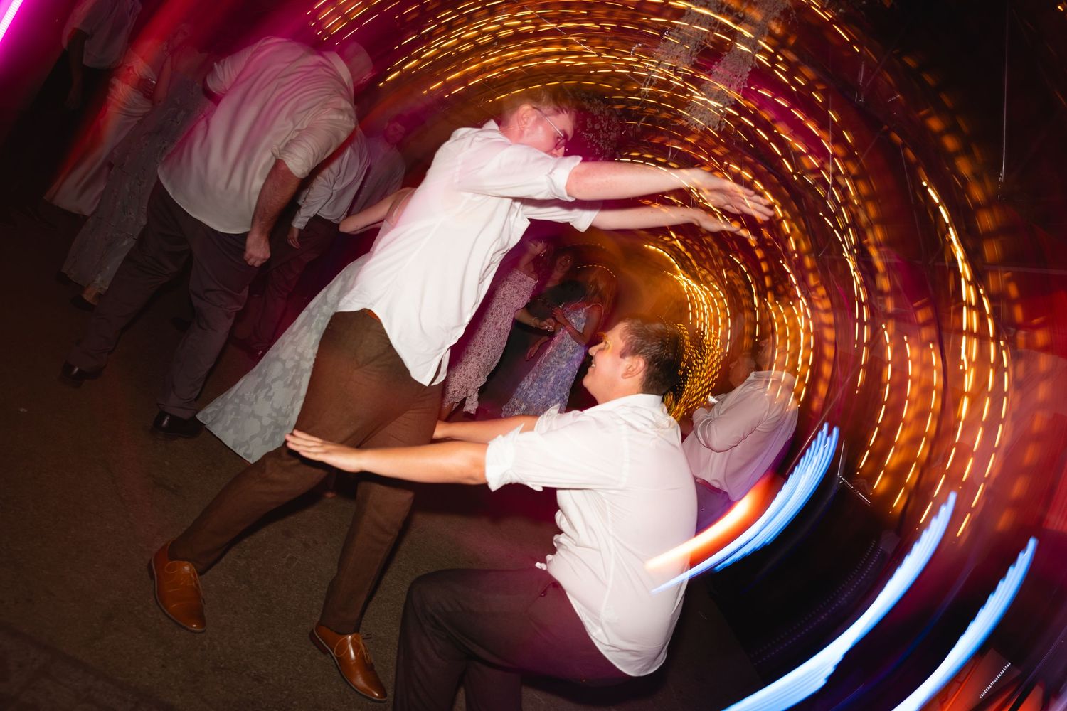 Long exposure photograph shows glowing light trails creating spiral patterns in dark room with motion blur effects.
