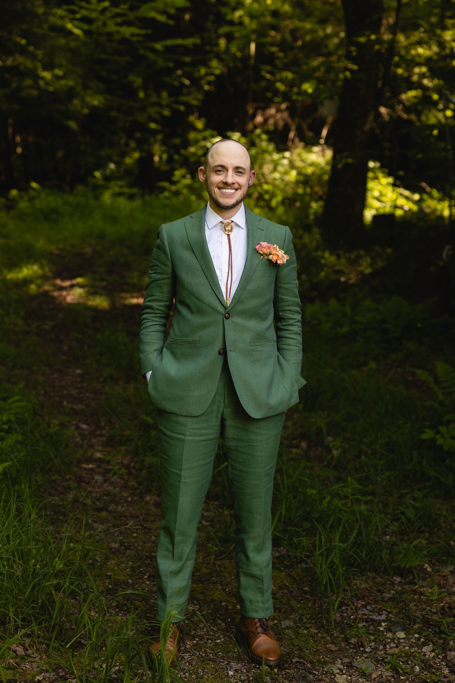 Someone wearing a stylish green suit poses confidently in a wooded outdoor setting with natural lighting.
