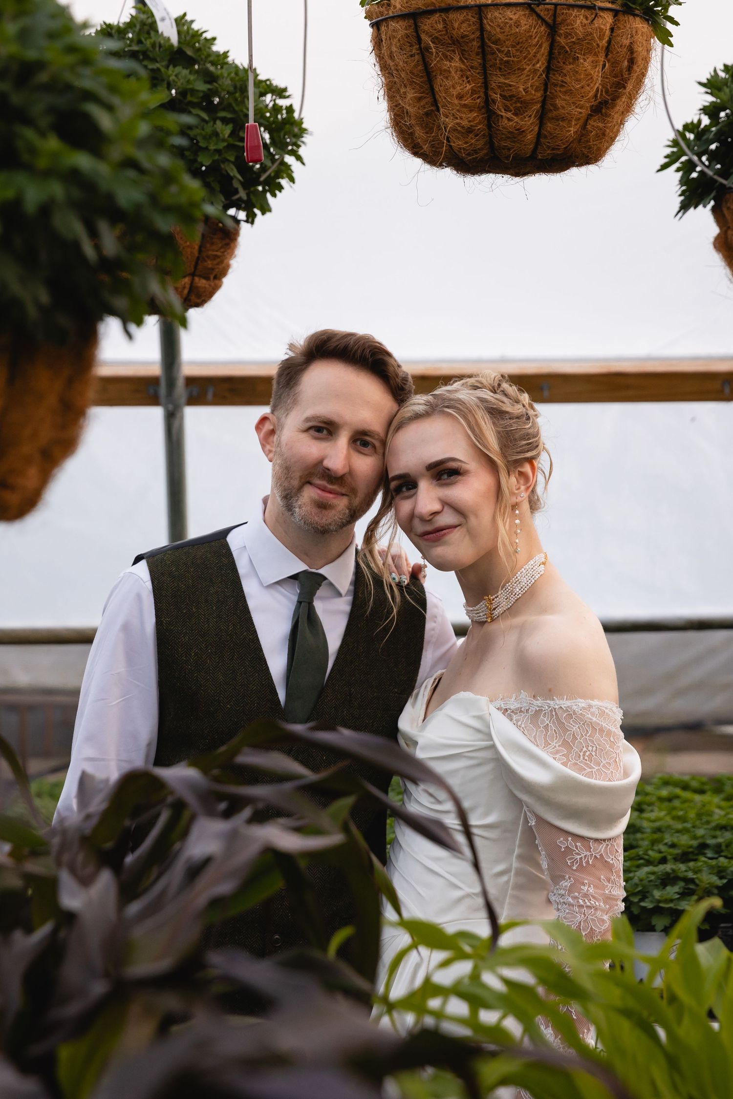 A romantic wedding couple shares an intimate moment together in a greenhouse setting with hanging plants.