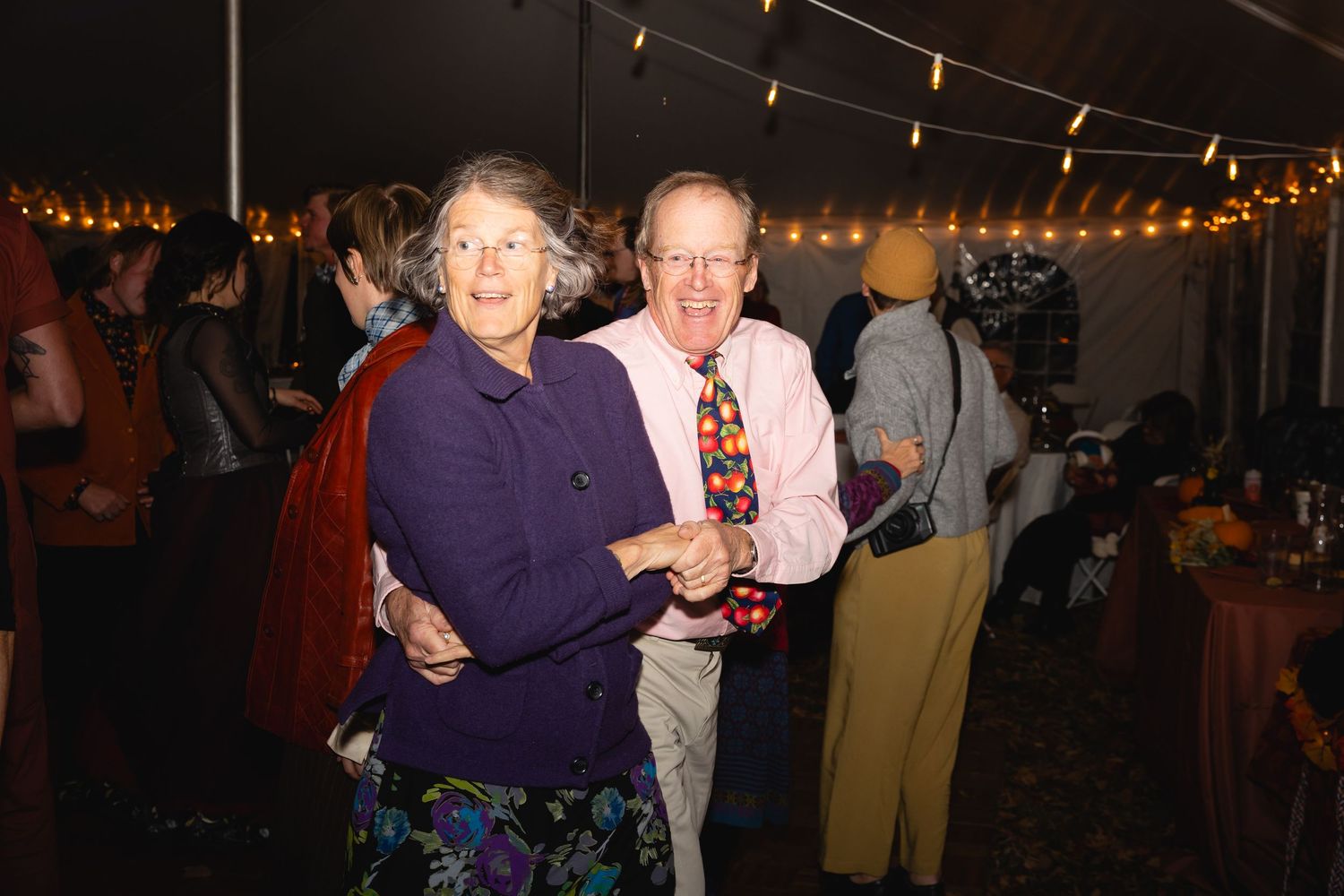 People dance together at a festive evening party with string lights illuminating the space.