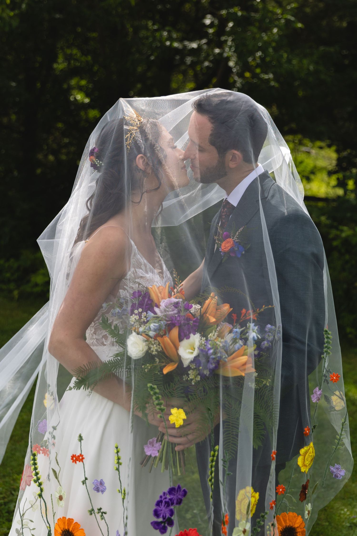 Wedding couple under floral-adorned veil in garden setting.