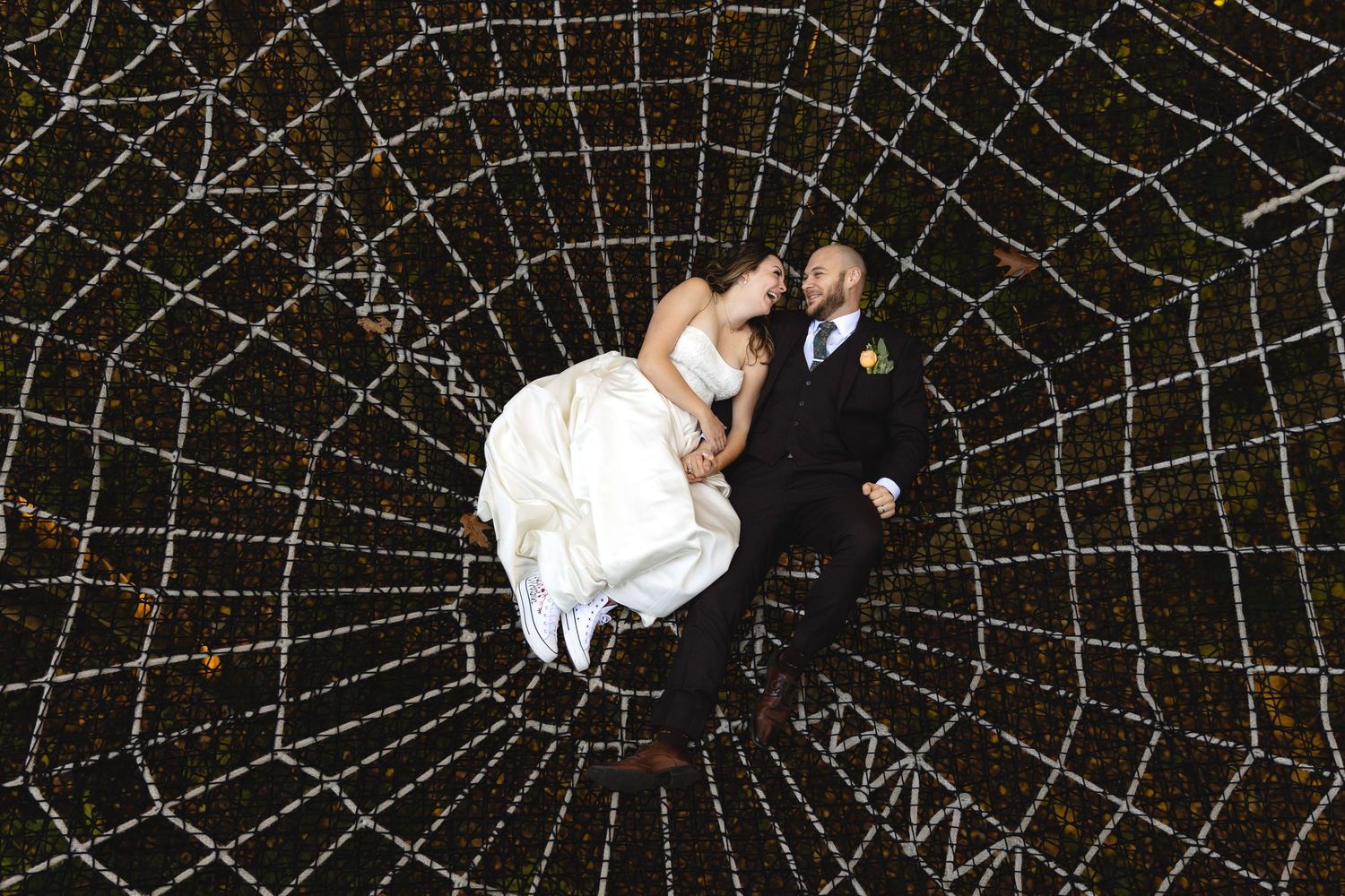 An overhead shot shows a couple lying on a giant decorative spider web structure at night.