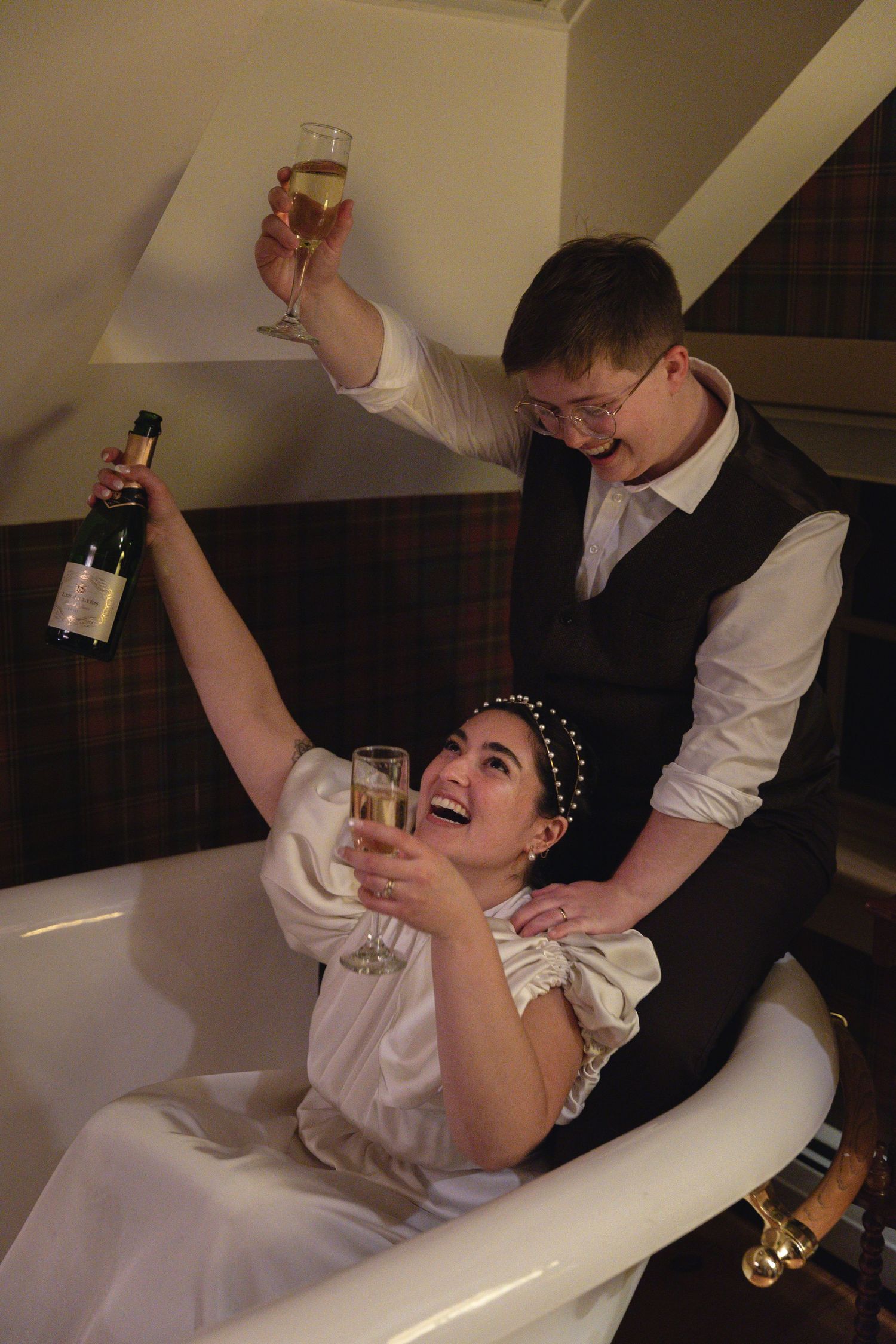 A joyful toast with champagne glasses raised high in a bathtub setting.