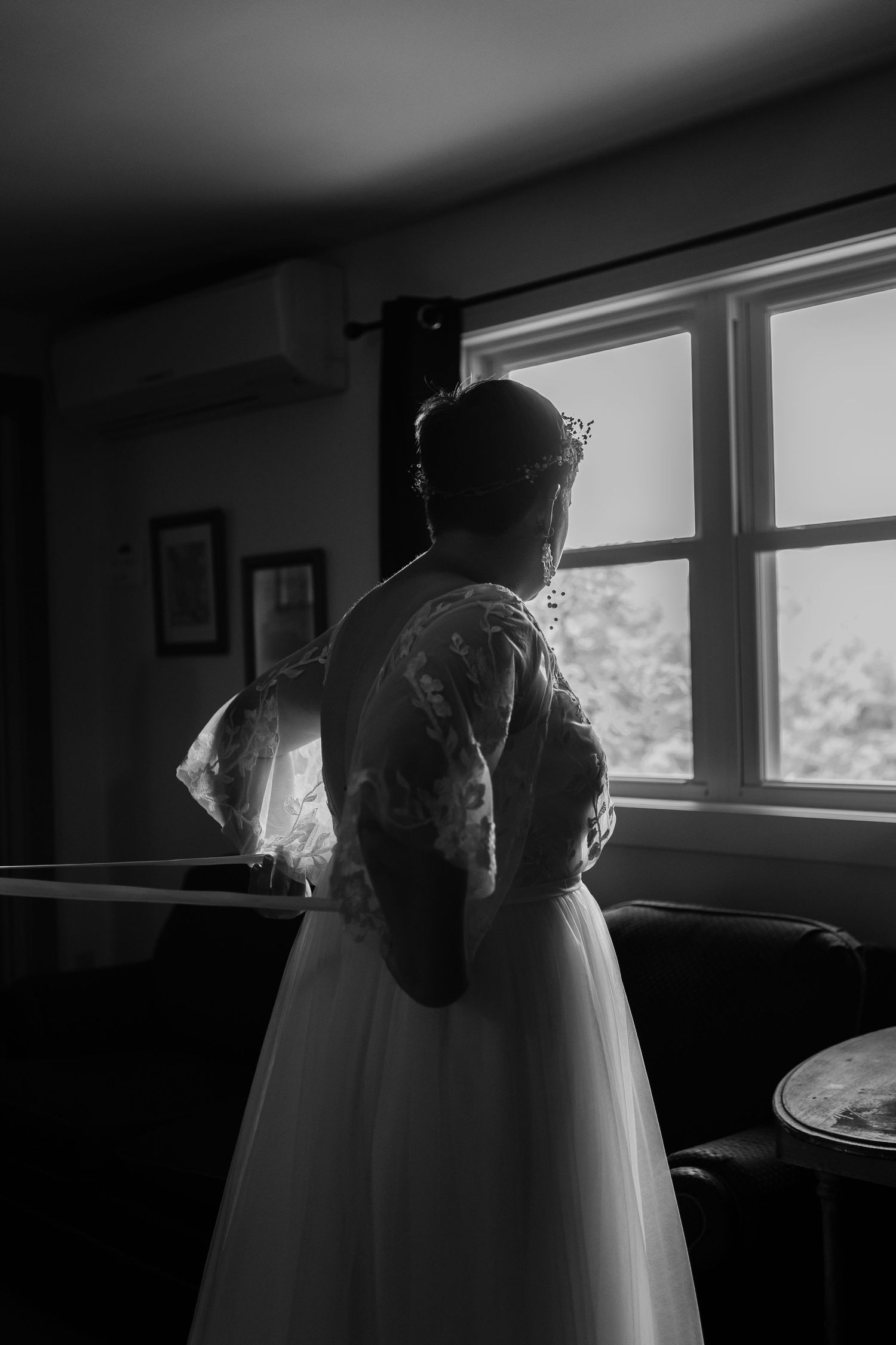 Silhouette of person in wedding dress standing by window in dark room.