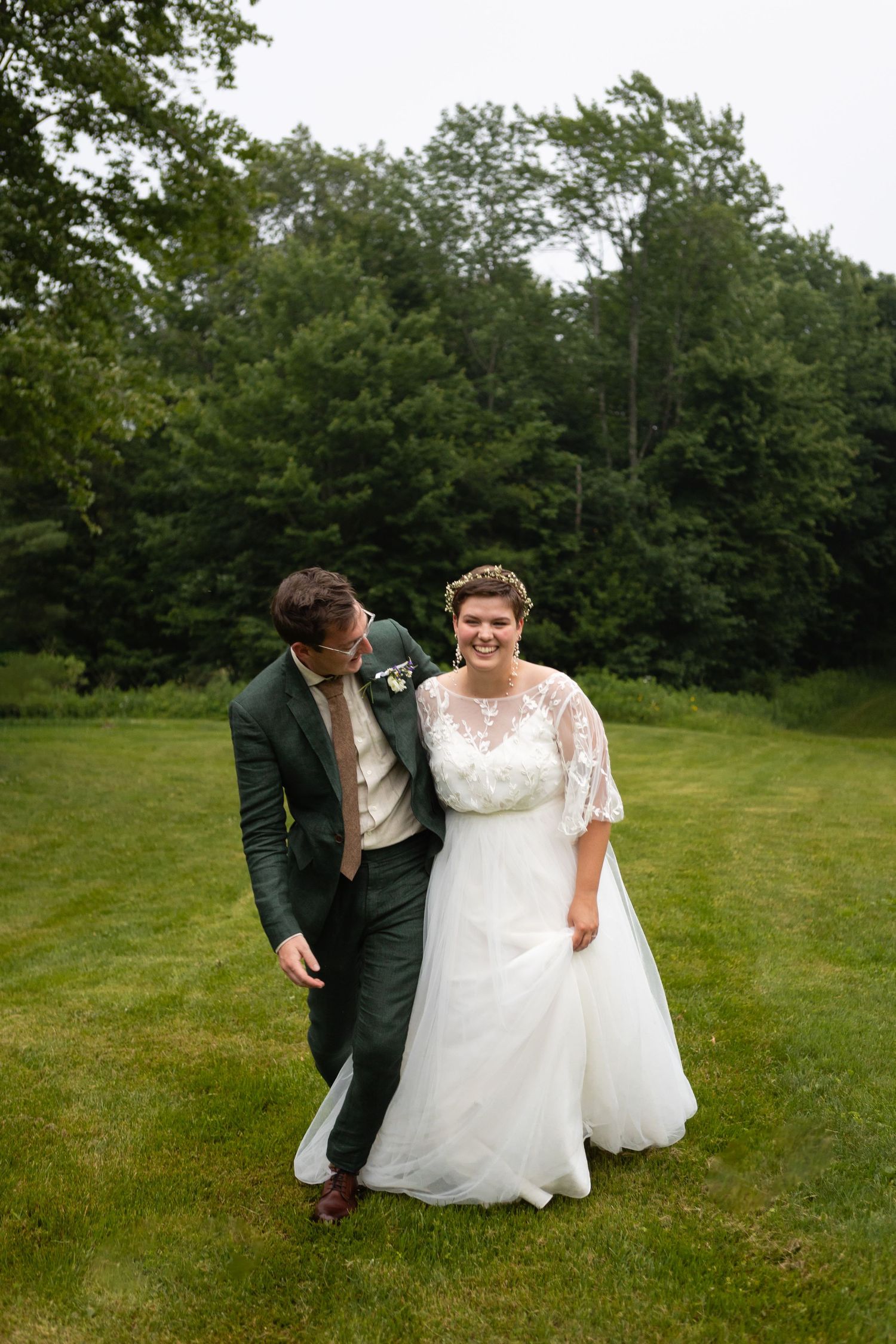 A couple shares a joyful moment on their wedding day while walking on a green lawn.