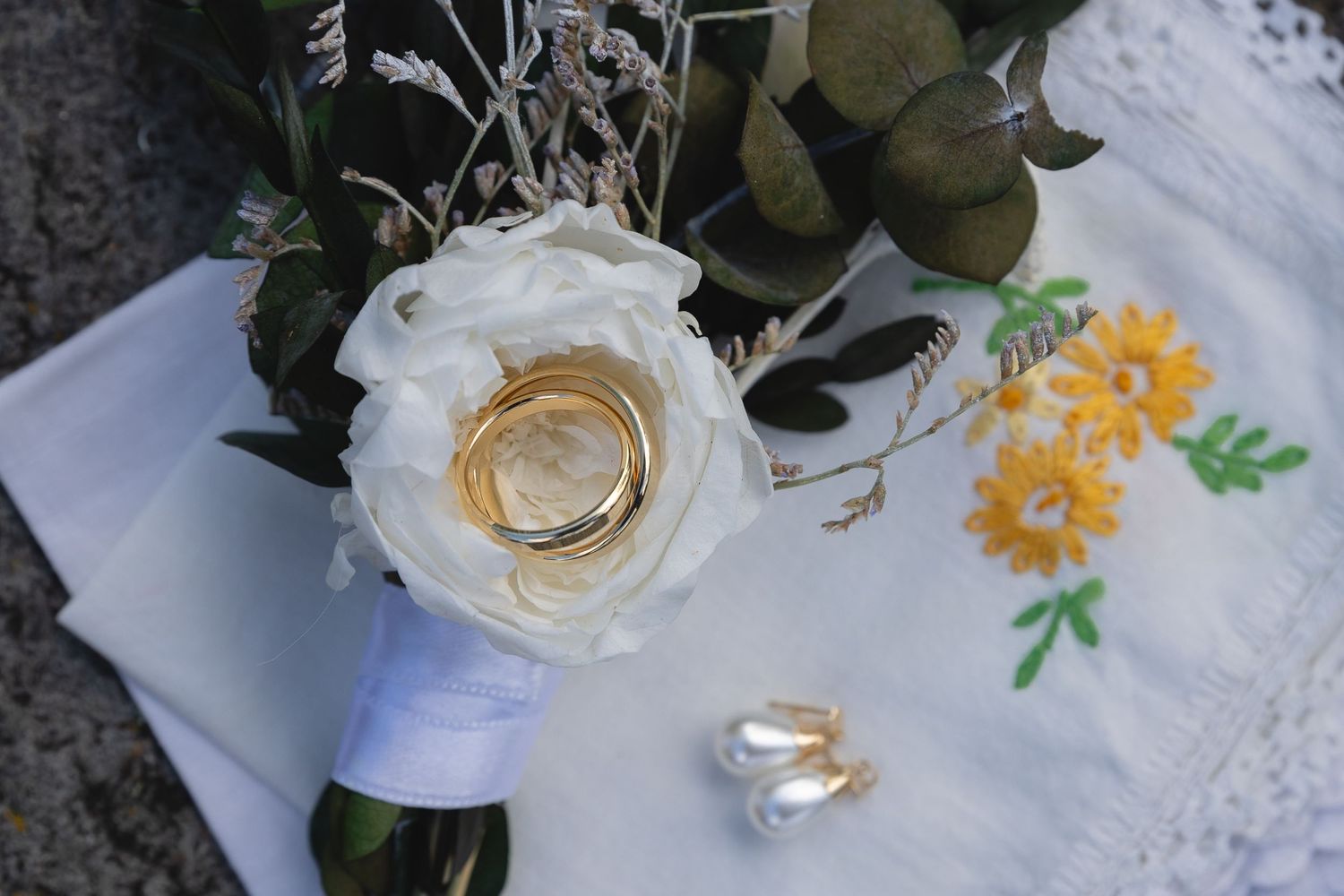Wedding rings nestled in a white rose with embroidered fabric detail.