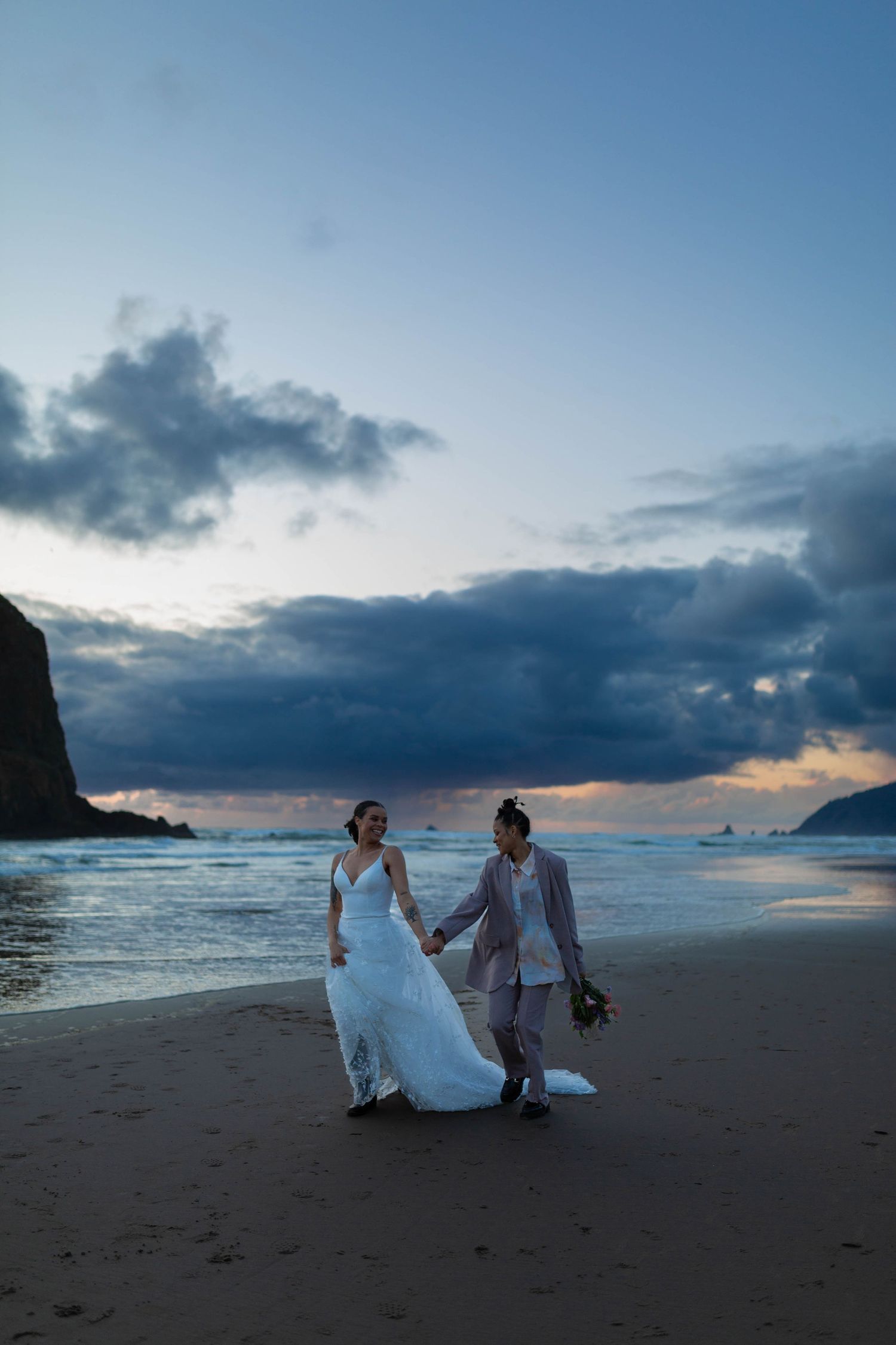 A couple walks together on a dramatic coastline beach during blue hour.