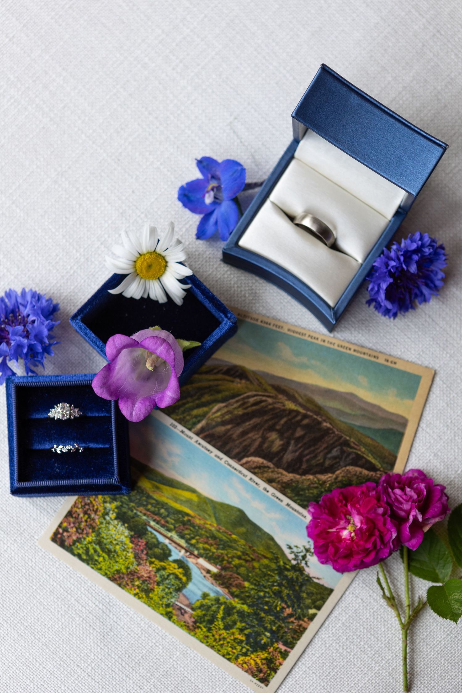 Wedding rings in blue boxes with fresh flowers and vintage postcards on white linen.