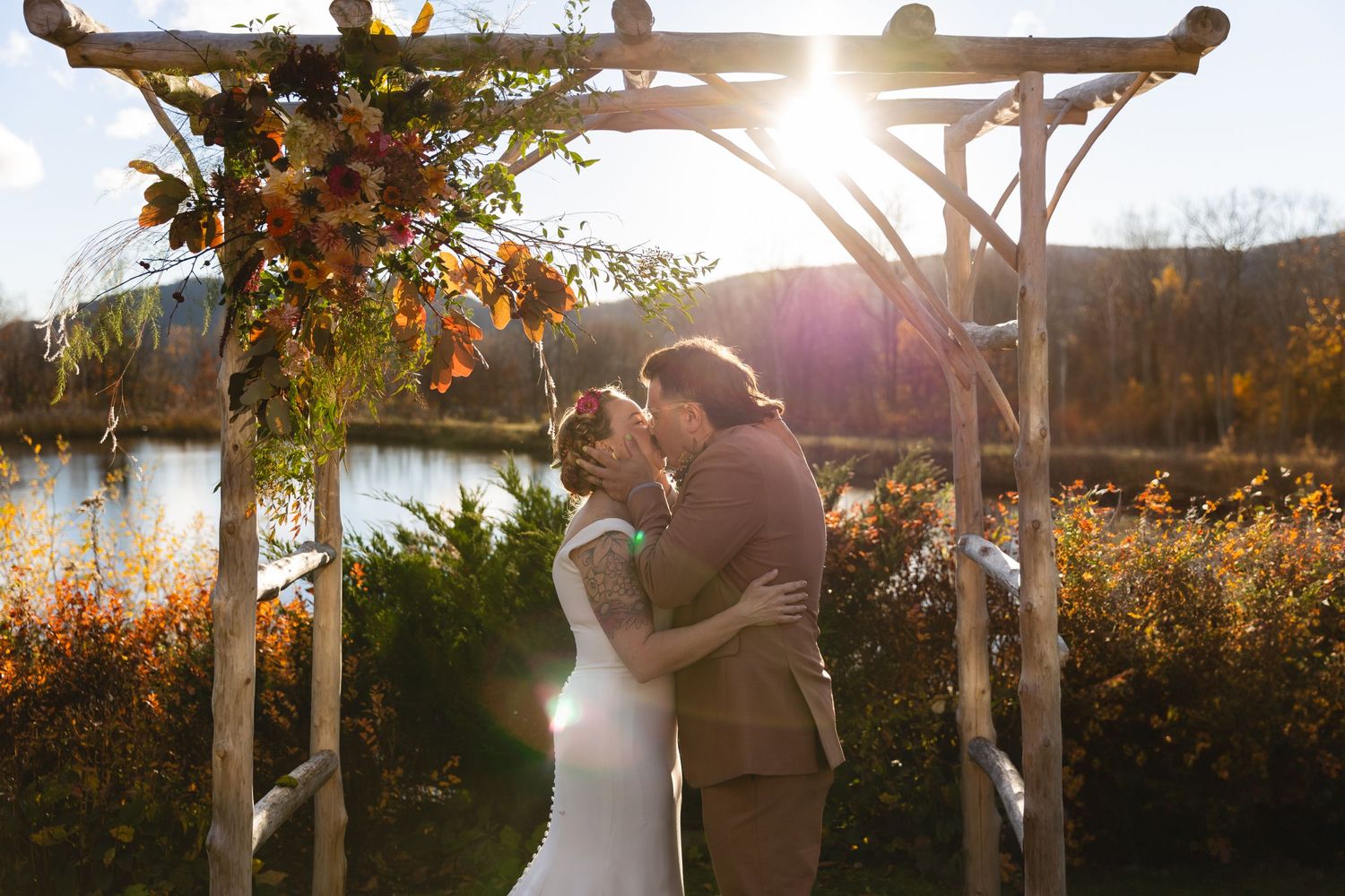 A romantic wedding kiss beneath a flower-adorned arch during golden hour.