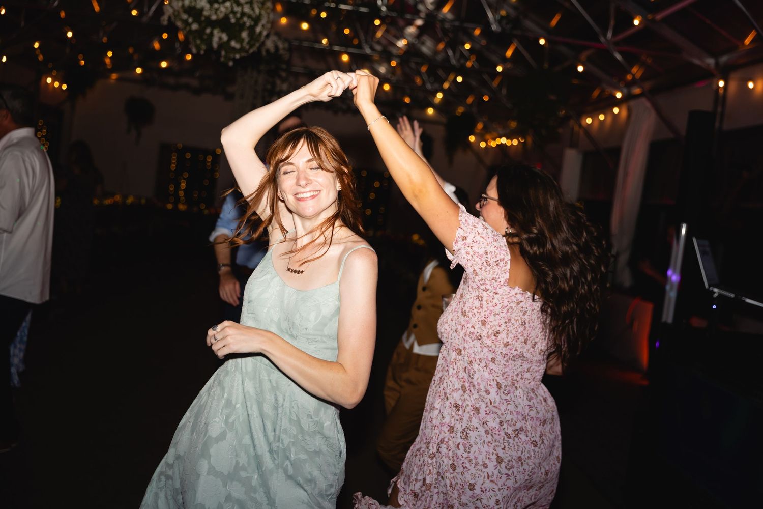 People dancing and celebrating at a dimly lit party venue with festive lights in the background.