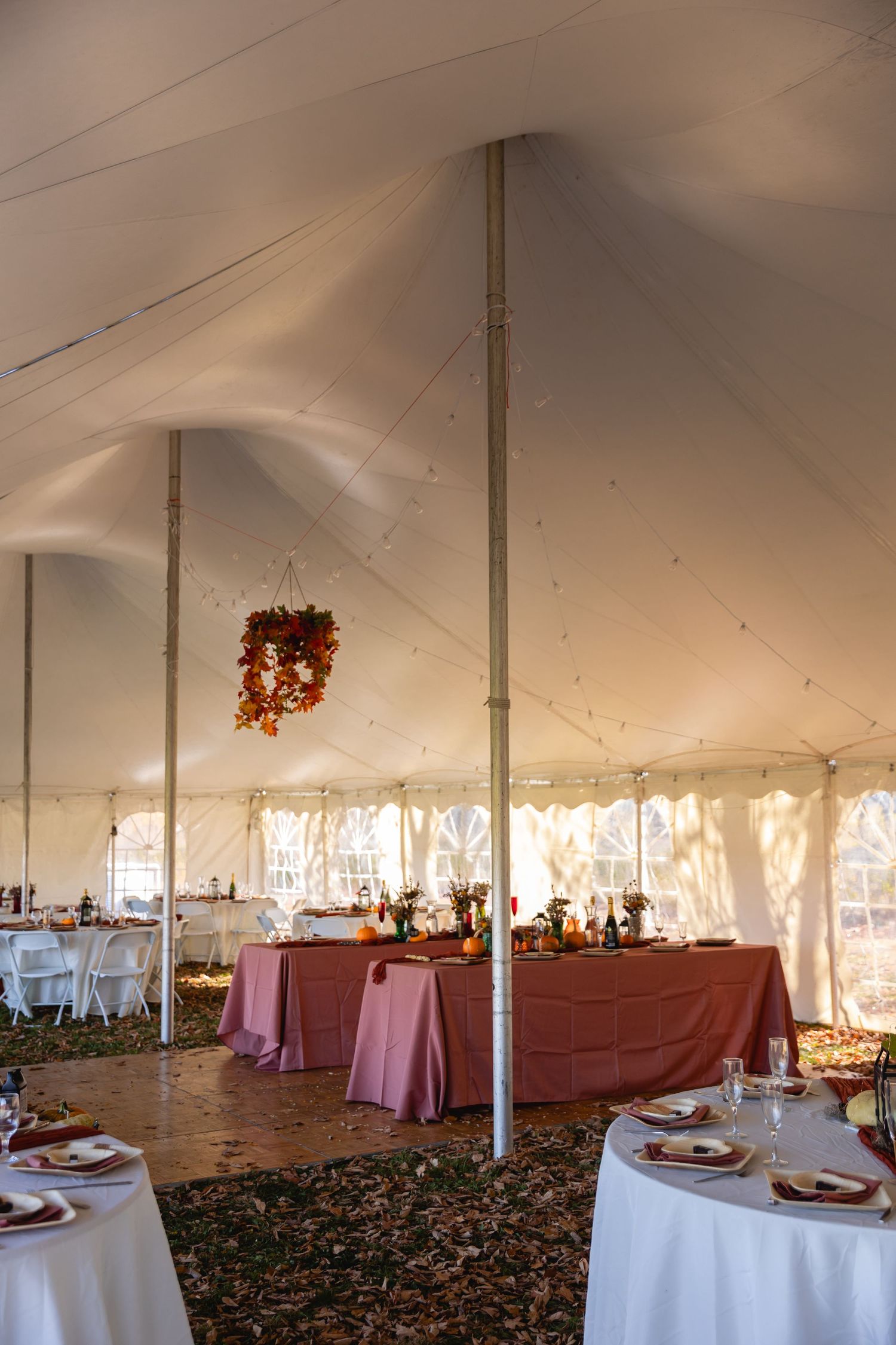 Interior of an elegant white wedding tent with round tables and pink tablecloths set for a formal reception.
