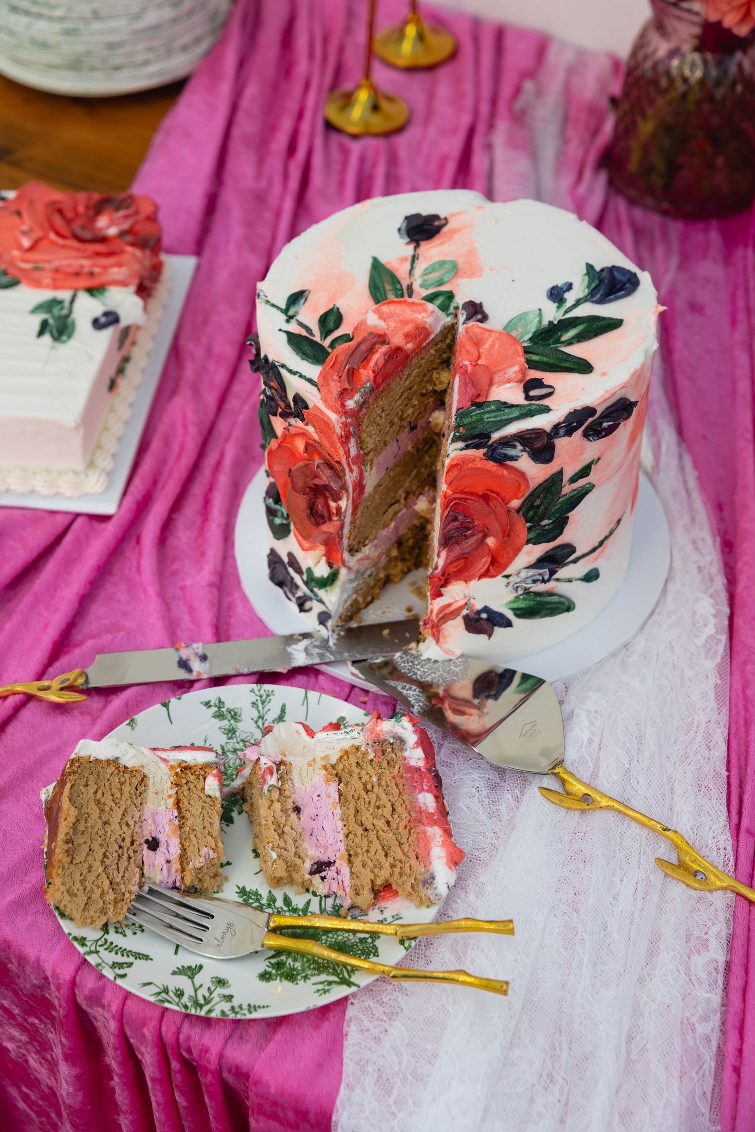 Partially eaten sandwich on decorative floral plate sits atop pink tablecloth with scattered crumbs and utensils.